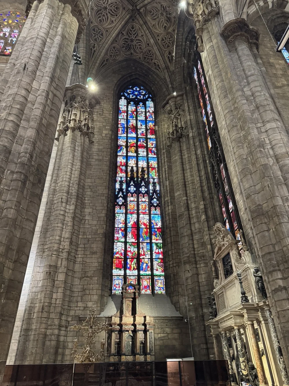 Colorful stained-glass window framed by Gothic stone columns inside Milan Cathedral