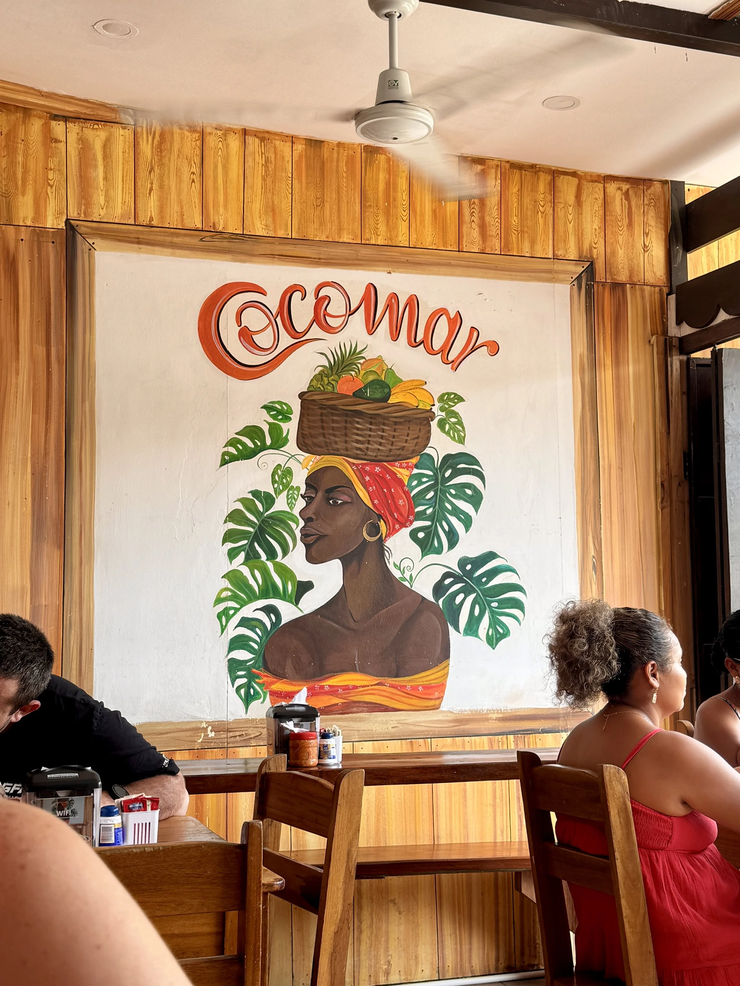 Interior wall mural at Cocomar Comida Caribeña with diners seated at tables.
