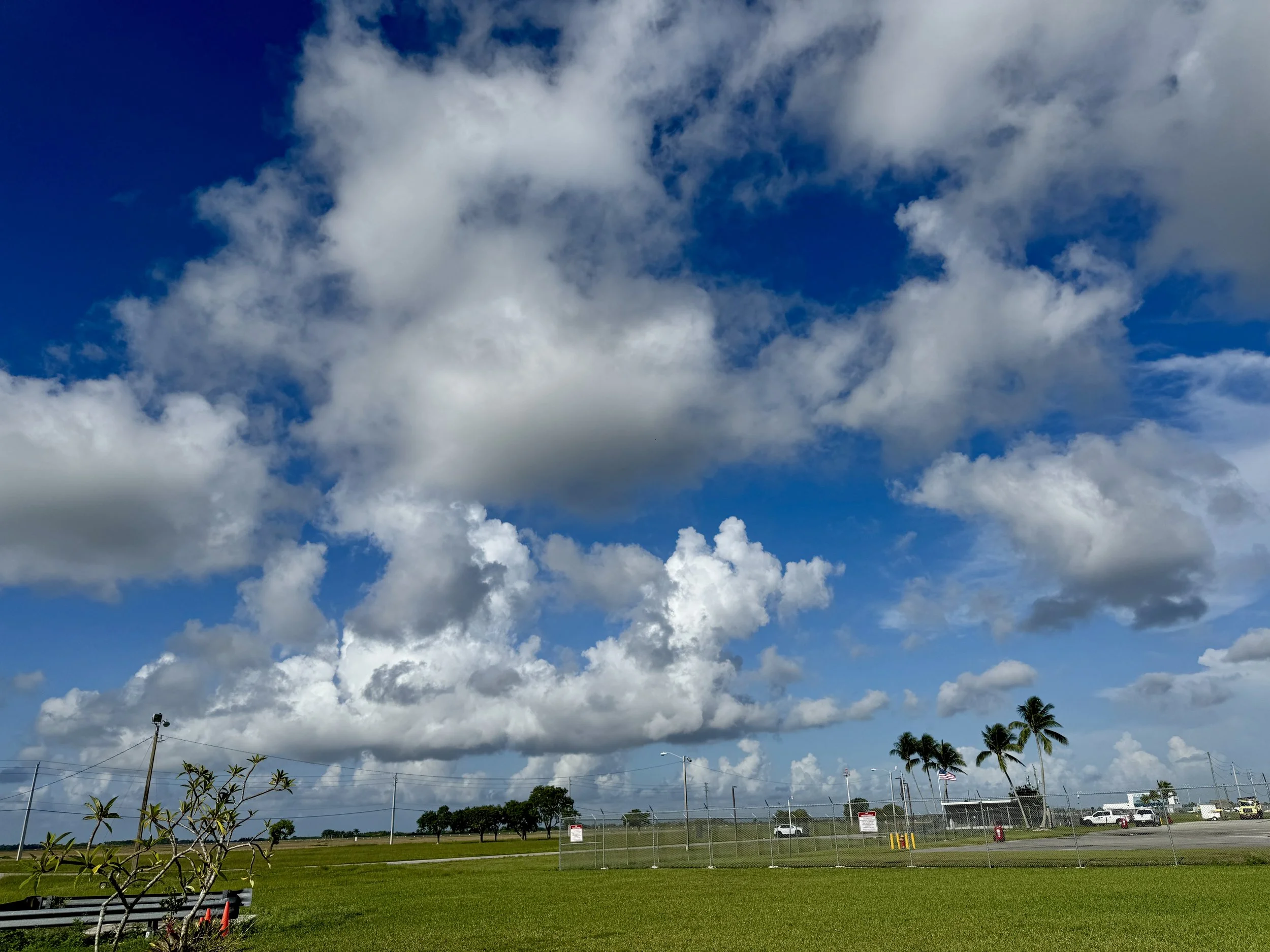view of the runway and grassy airfield under a large puffy clouds at Skydive Miami
