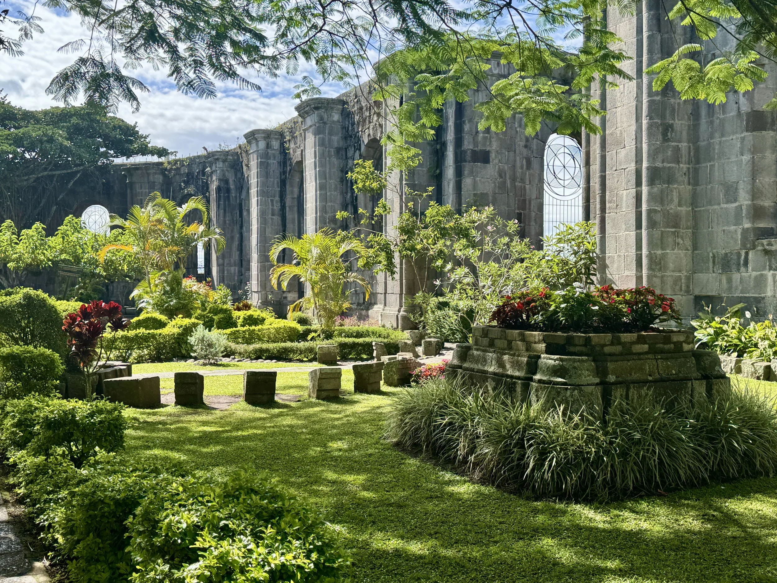 Interior garden courtyard inside the Cartago ruins with manicured hedges, flowers, and tall stone walls.