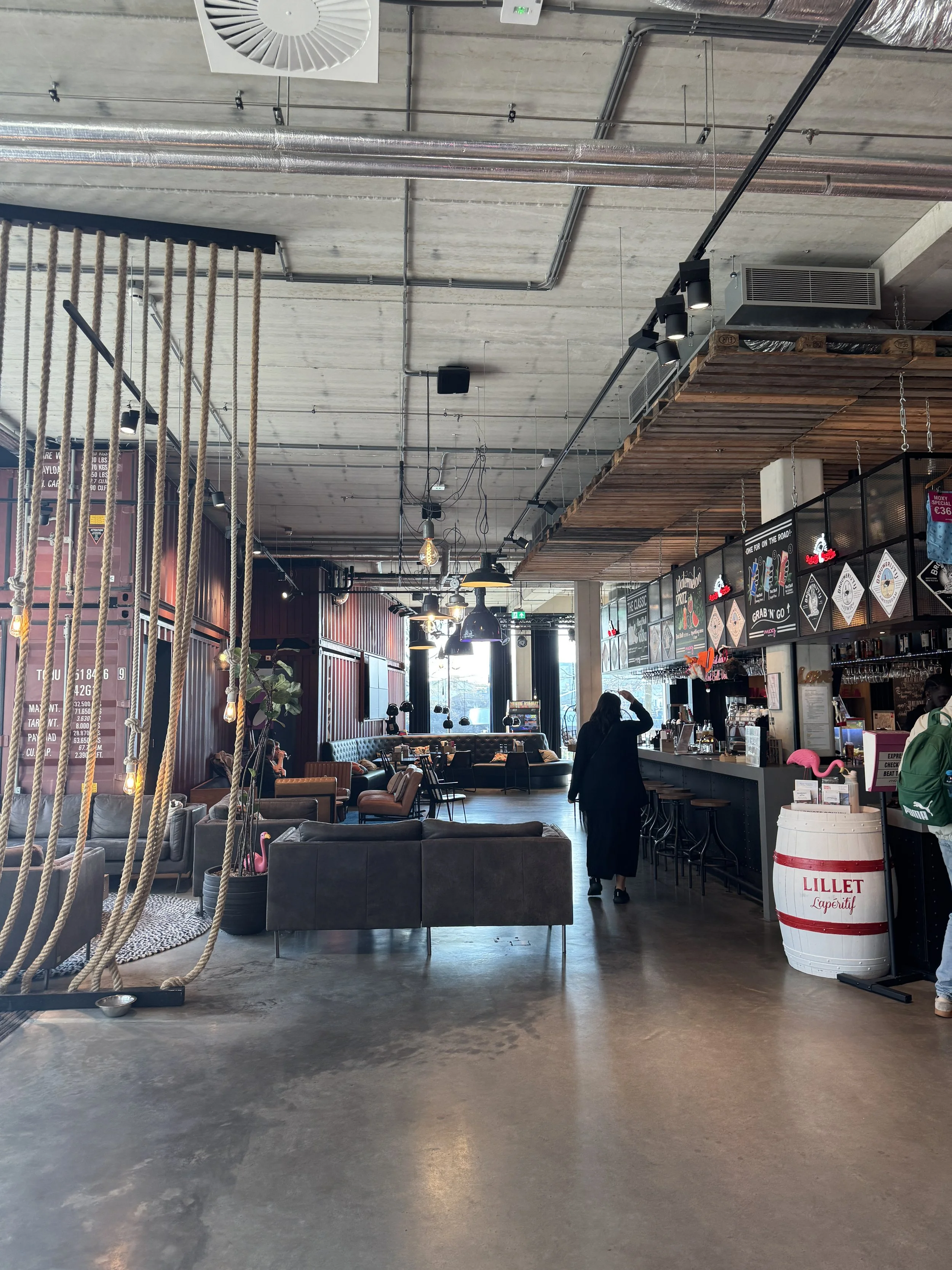 Industrial-style interior of Moxy Amsterdam hotel featuring bar area, seating, and exposed ceiling design