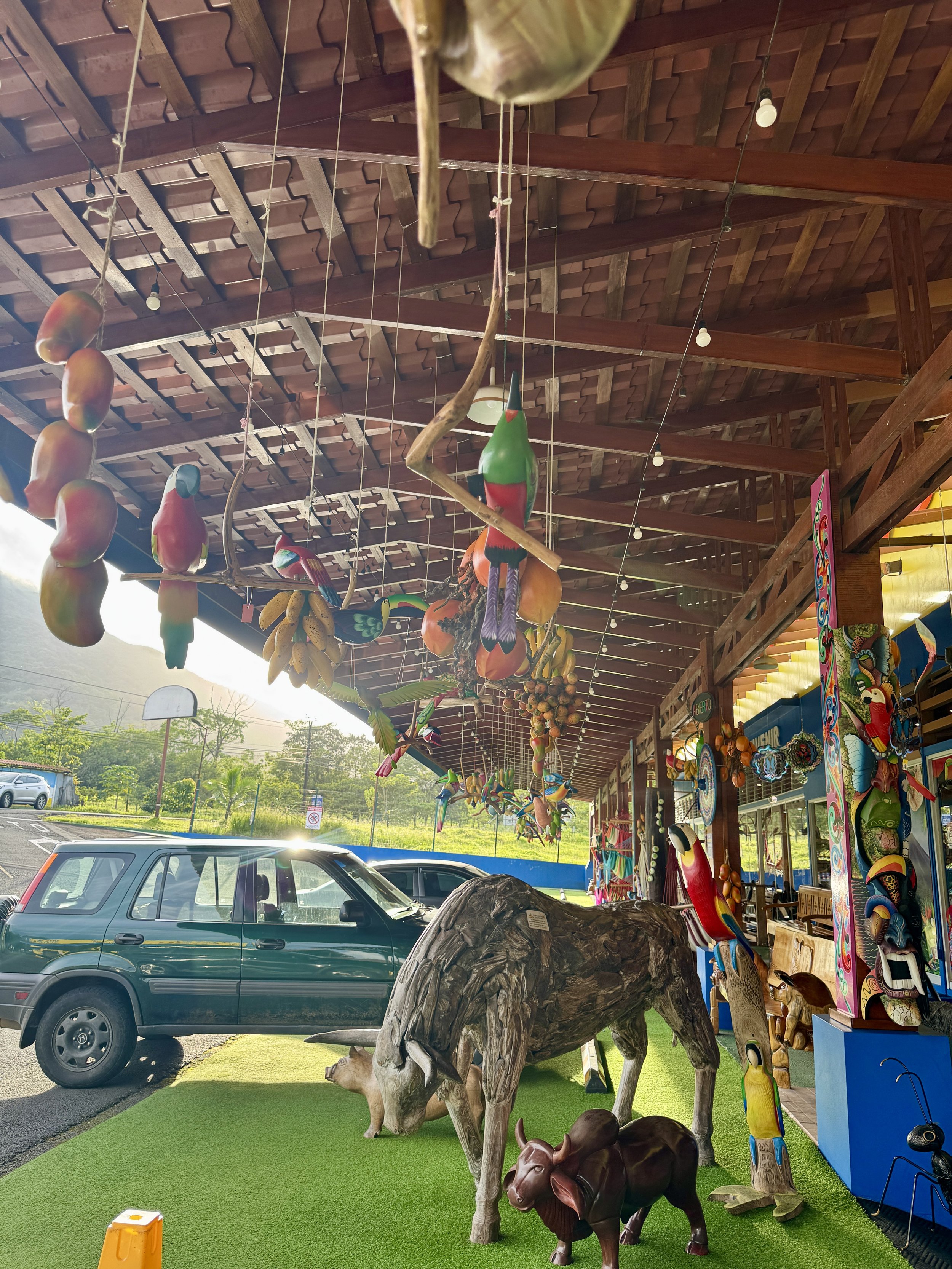 Open-air souvenir shop display with hanging crafts and a cow statue near the entrance.