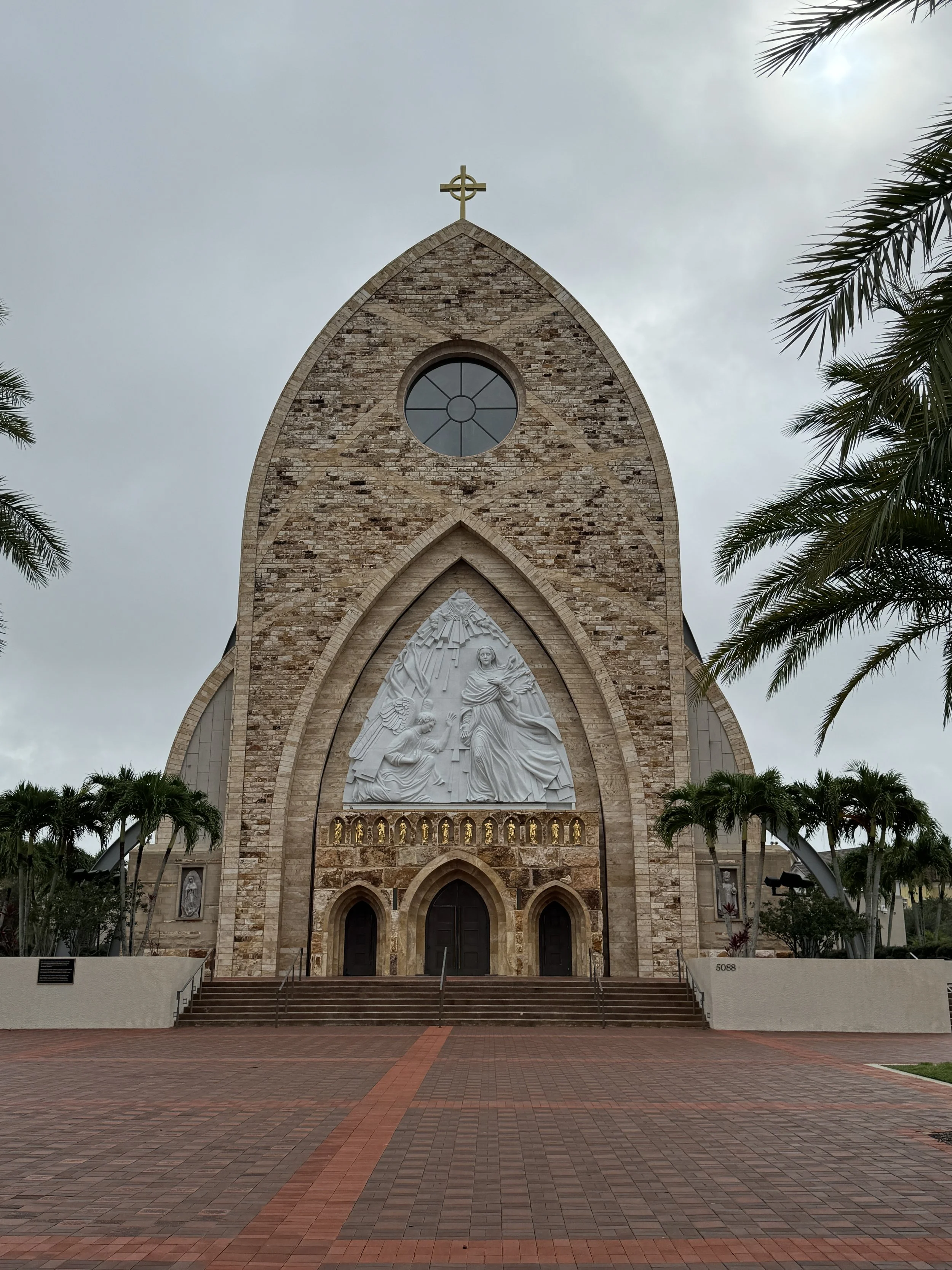 Front view of Ave Maria Catholic Parish Church with arched stone façade and religious sculpture above the entrance in Ave Maria, Florida.