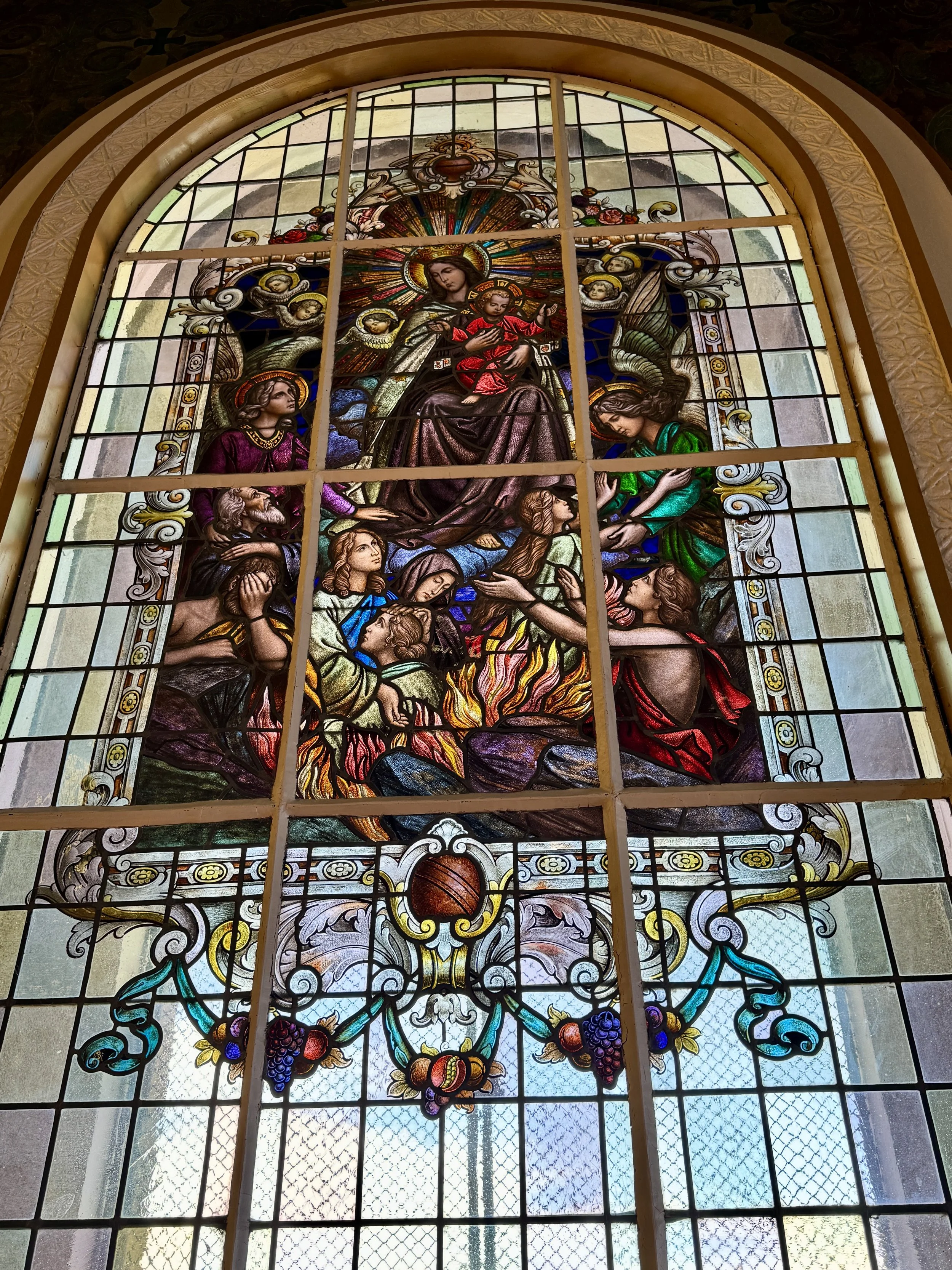Colorful stained glass window inside Basílica de Nuestra Señora de los Ángeles depicting a religious scene.