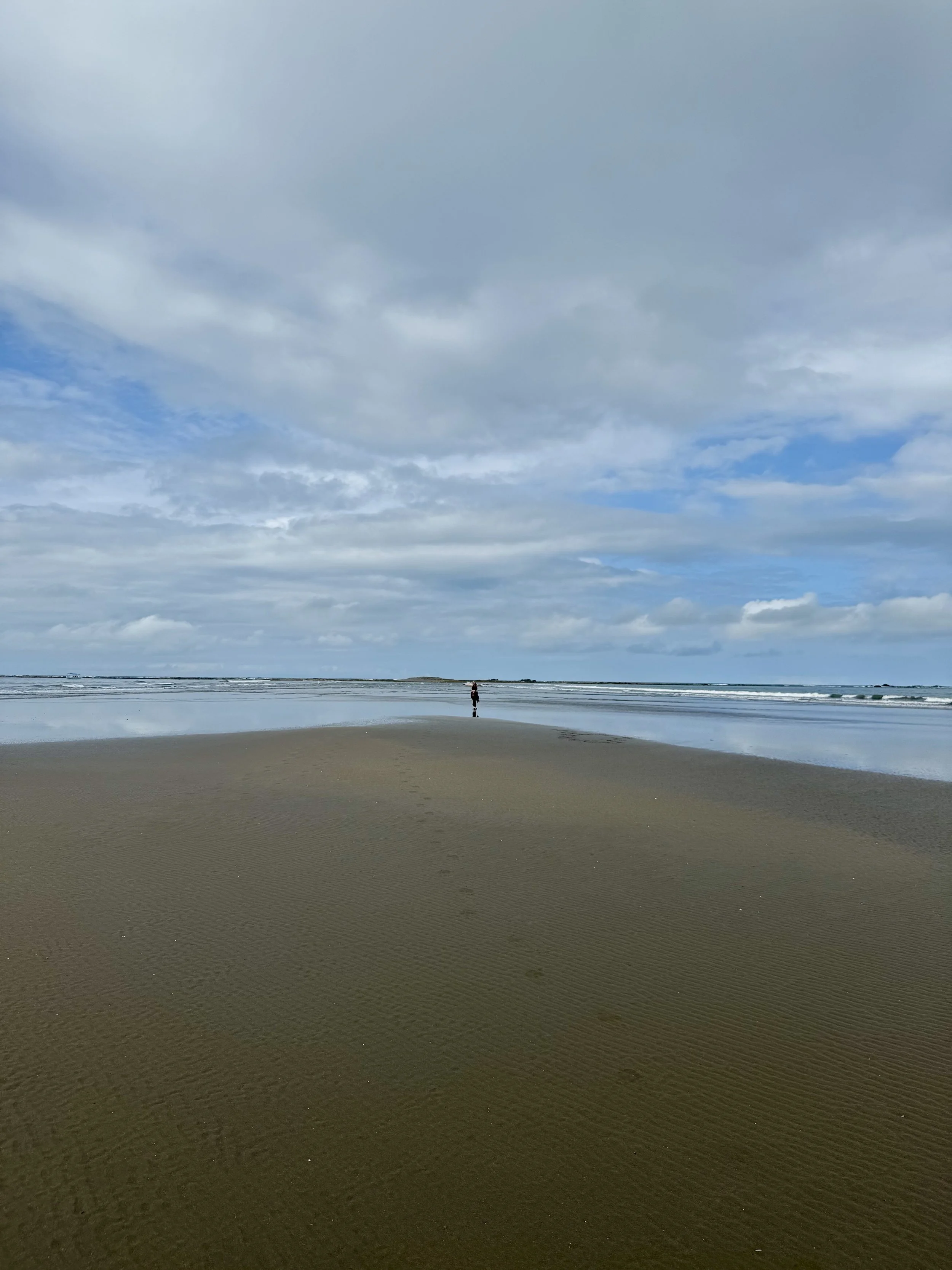 Expansive flat beach with a lone person walking in the distance under partly cloudy skies.