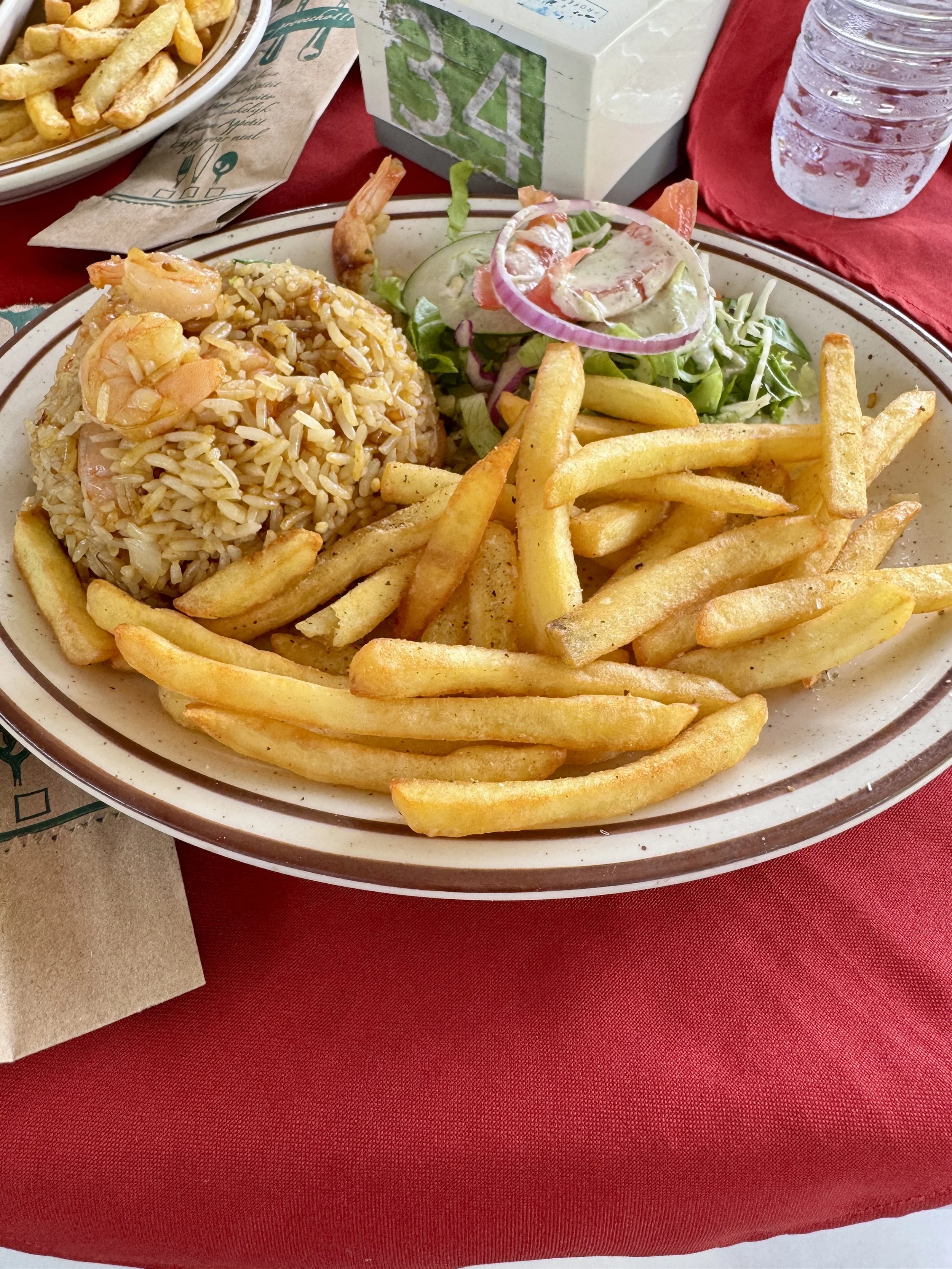 Plate of shrimp rice served with French fries, salad, and a drink at the open-air restaurant.