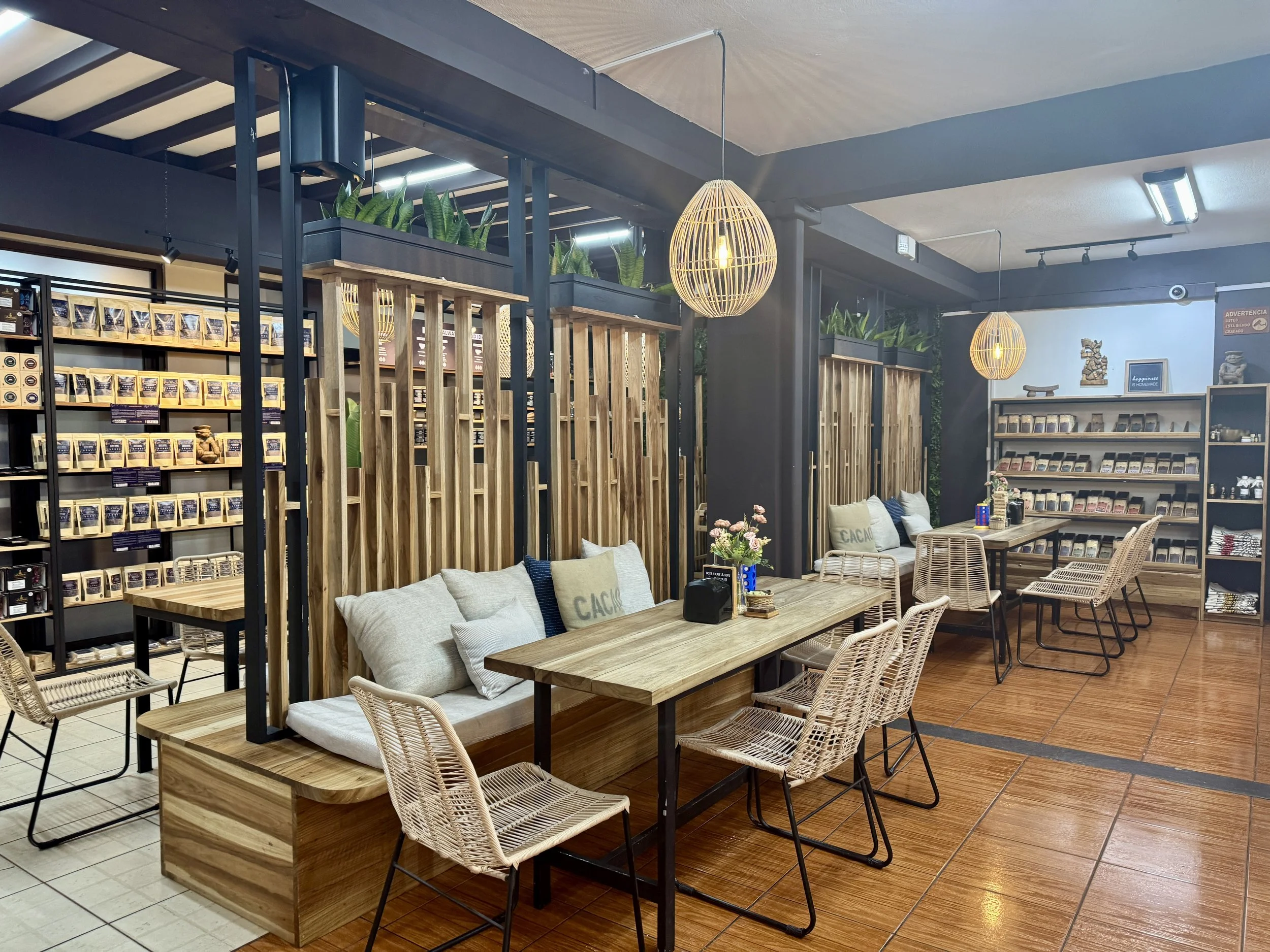 Cozy dessert shop seating area with wooden tables, hanging lights, and shelves filled with packaged sweets.