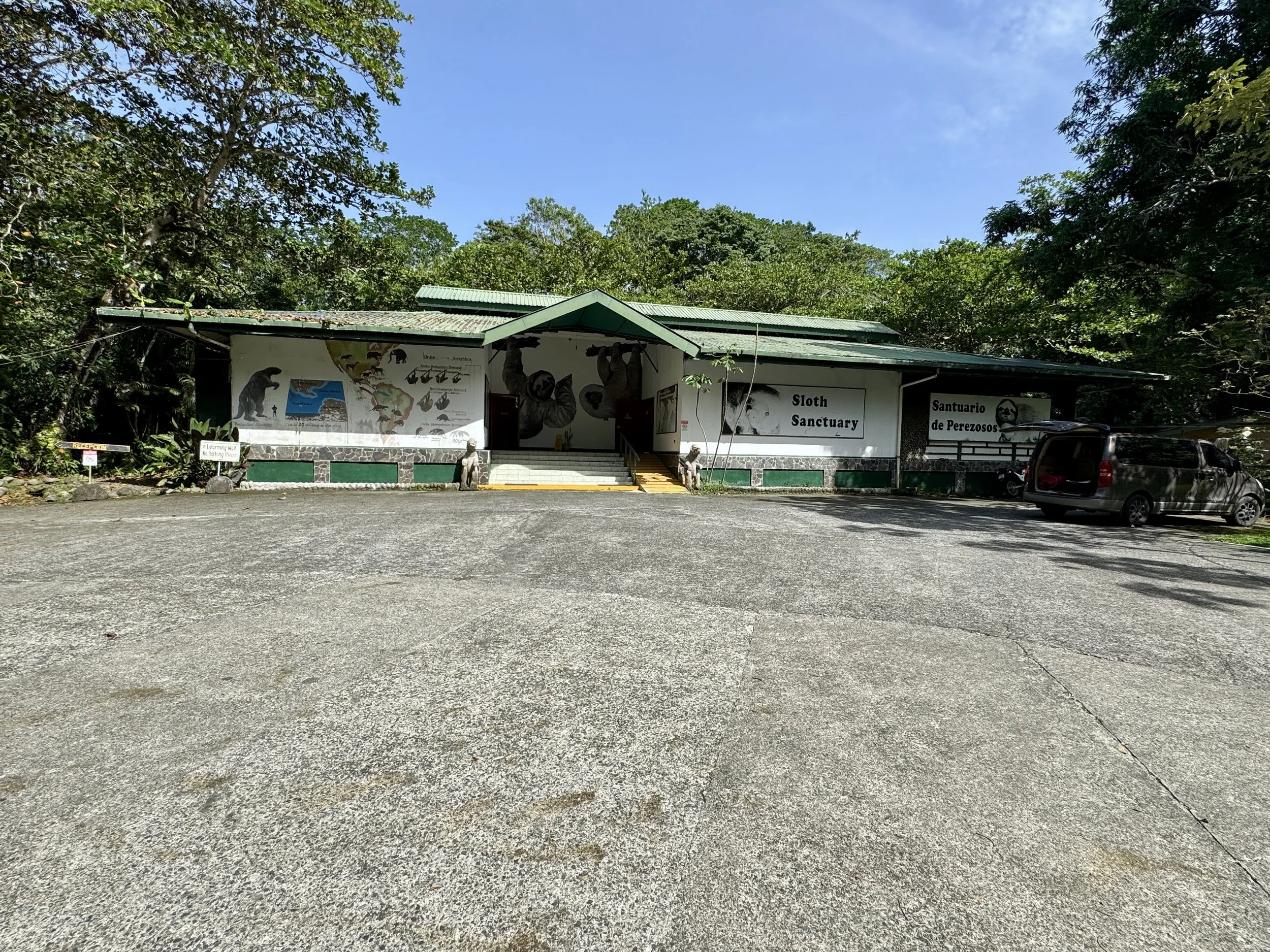 Entrance area of the Sloth Sanctuary in Limón with open gravel lot and buildings.
