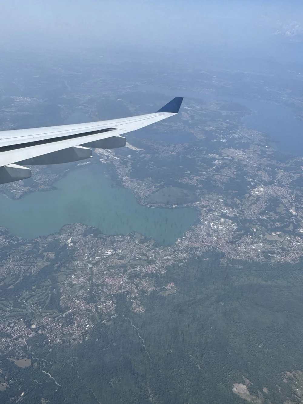 Airplane wing above lakes and towns in northern Italy during the approach to Milan.