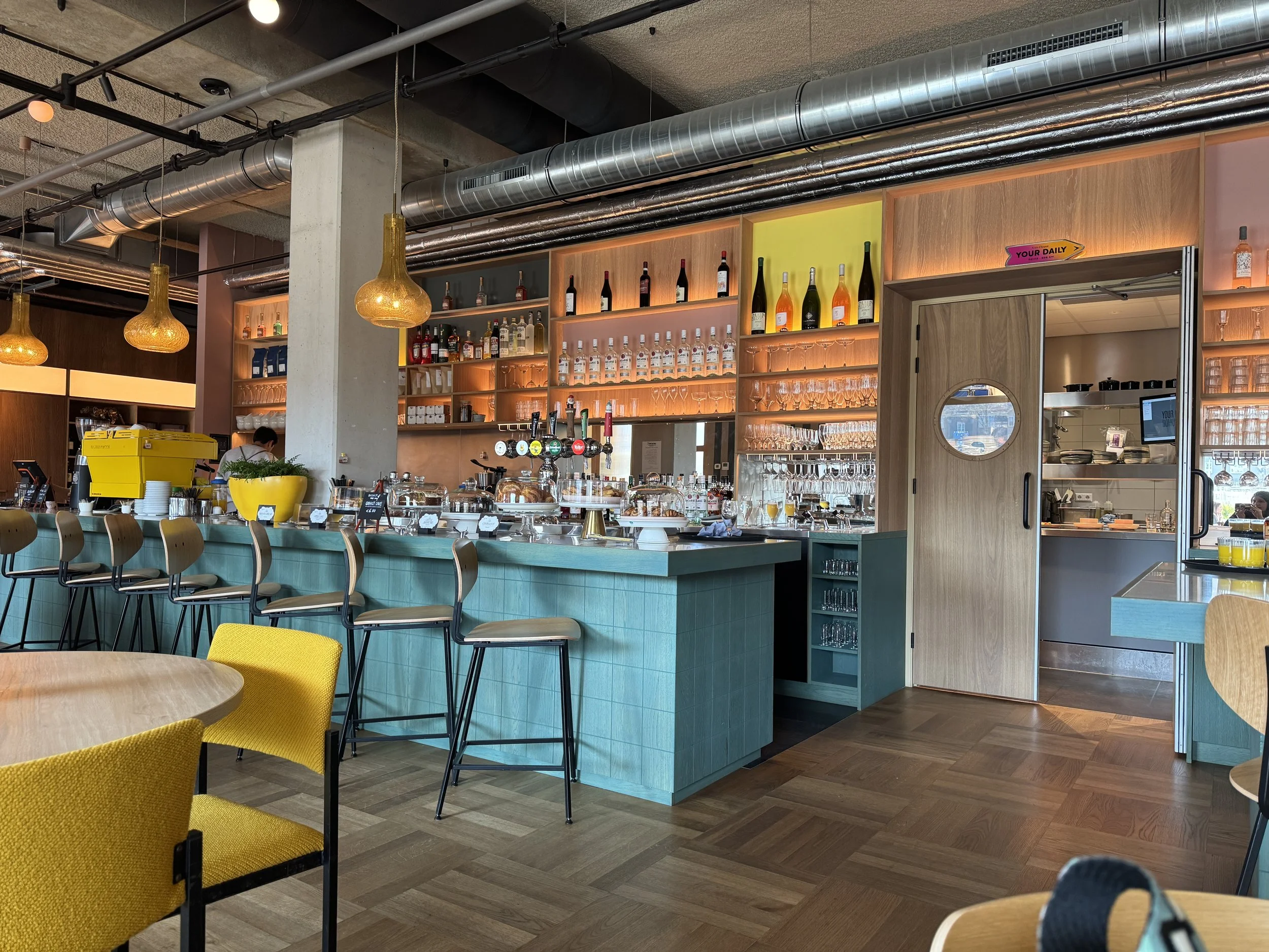 Modern interior of Your Daily Domus restaurant in Amsterdam with bar seating, teal counters, and warm lighting