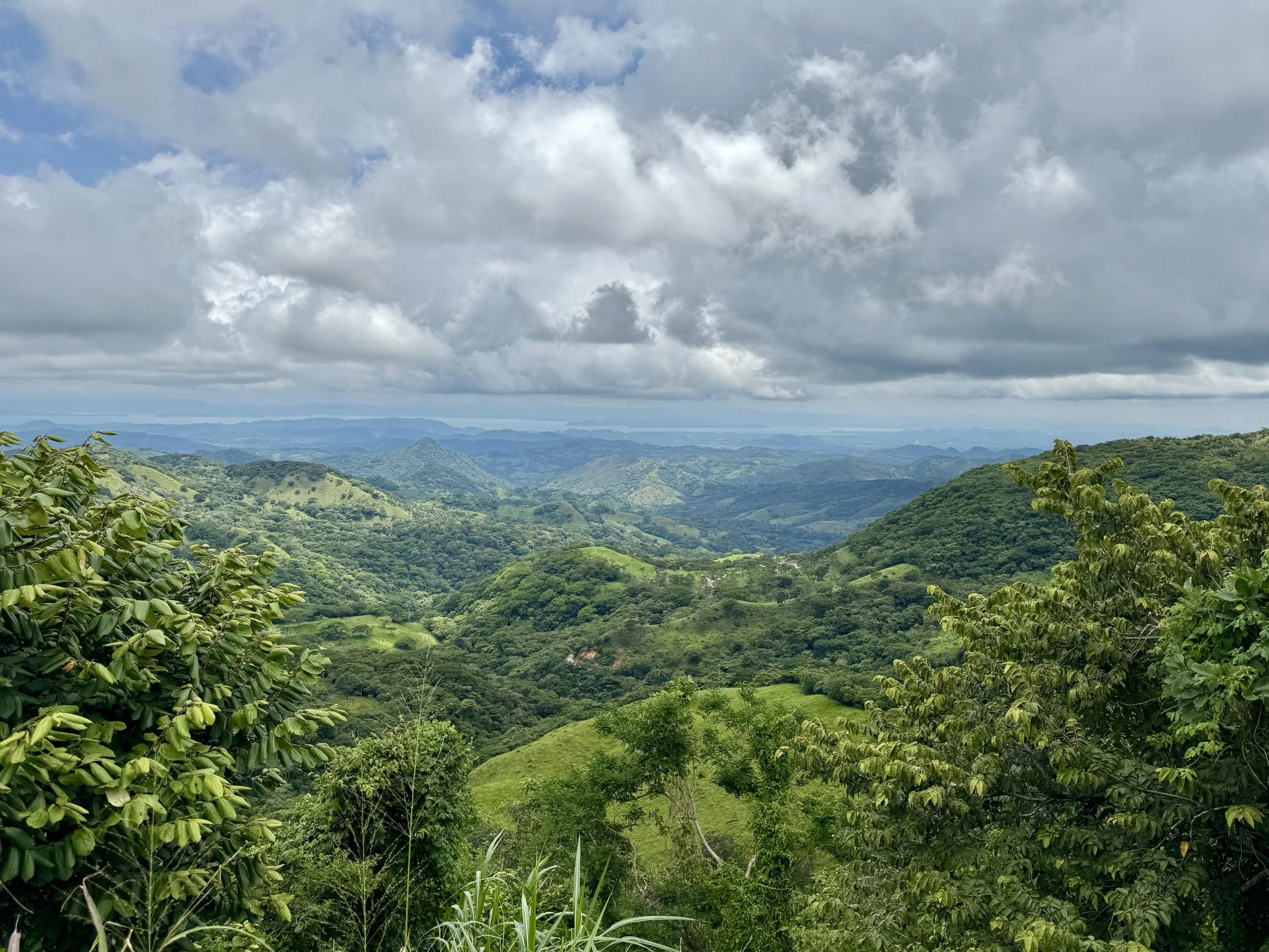 Panoramic view of rolling green hills and valleys under dramatic cloudy skies, photographed from a roadside pull-off.