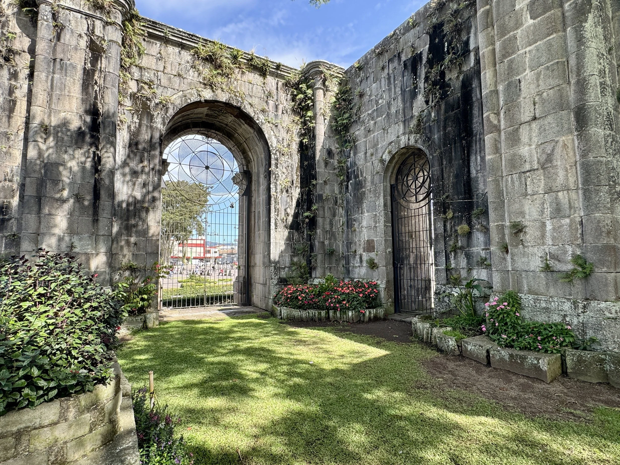 Sunlit stone archway inside the Santiago Apóstol ruins with greenery and blue sky beyond.