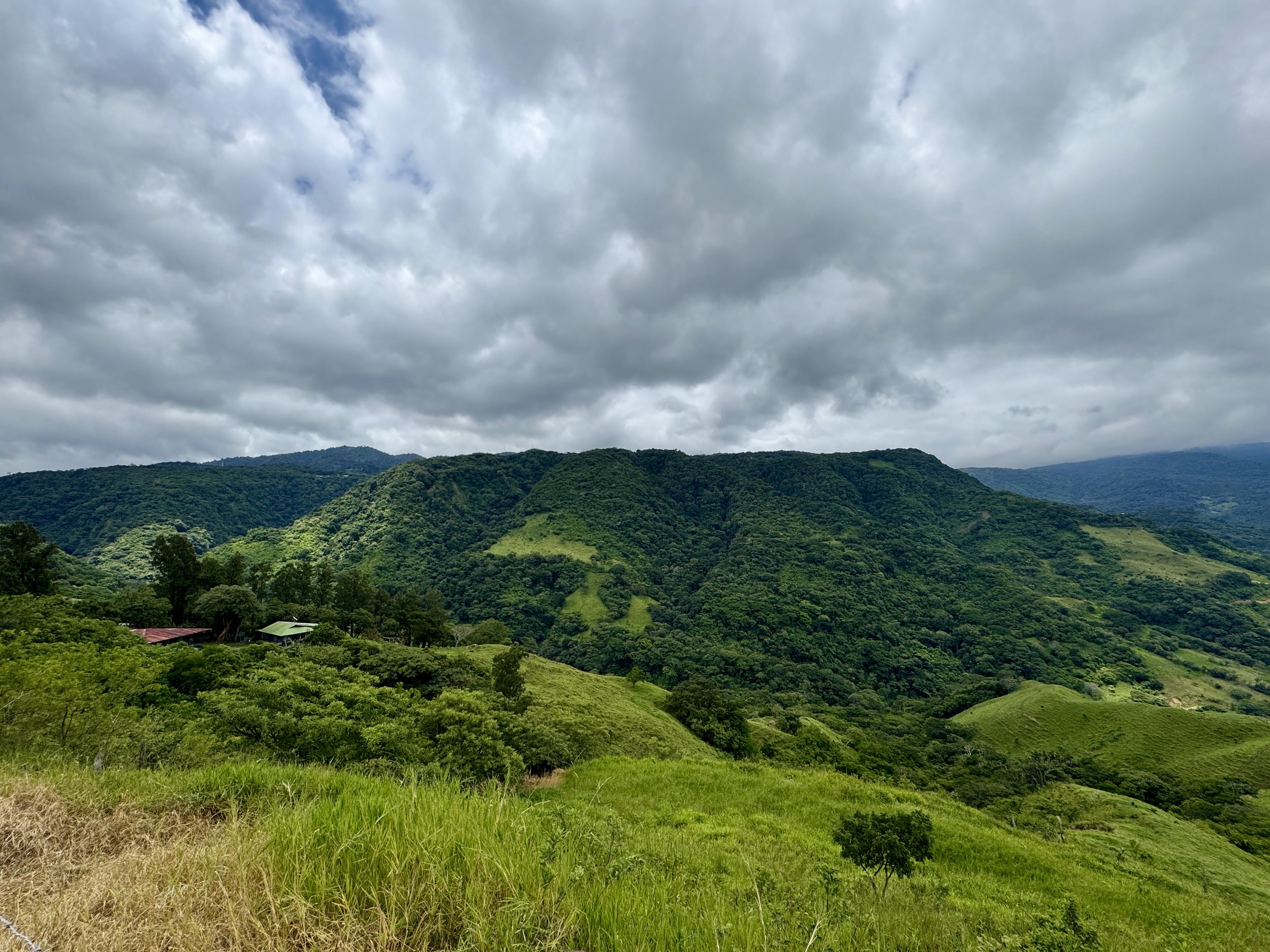 Lush mountain landscape with layered hills and patches of farmland seen from a scenic roadside viewpoint.