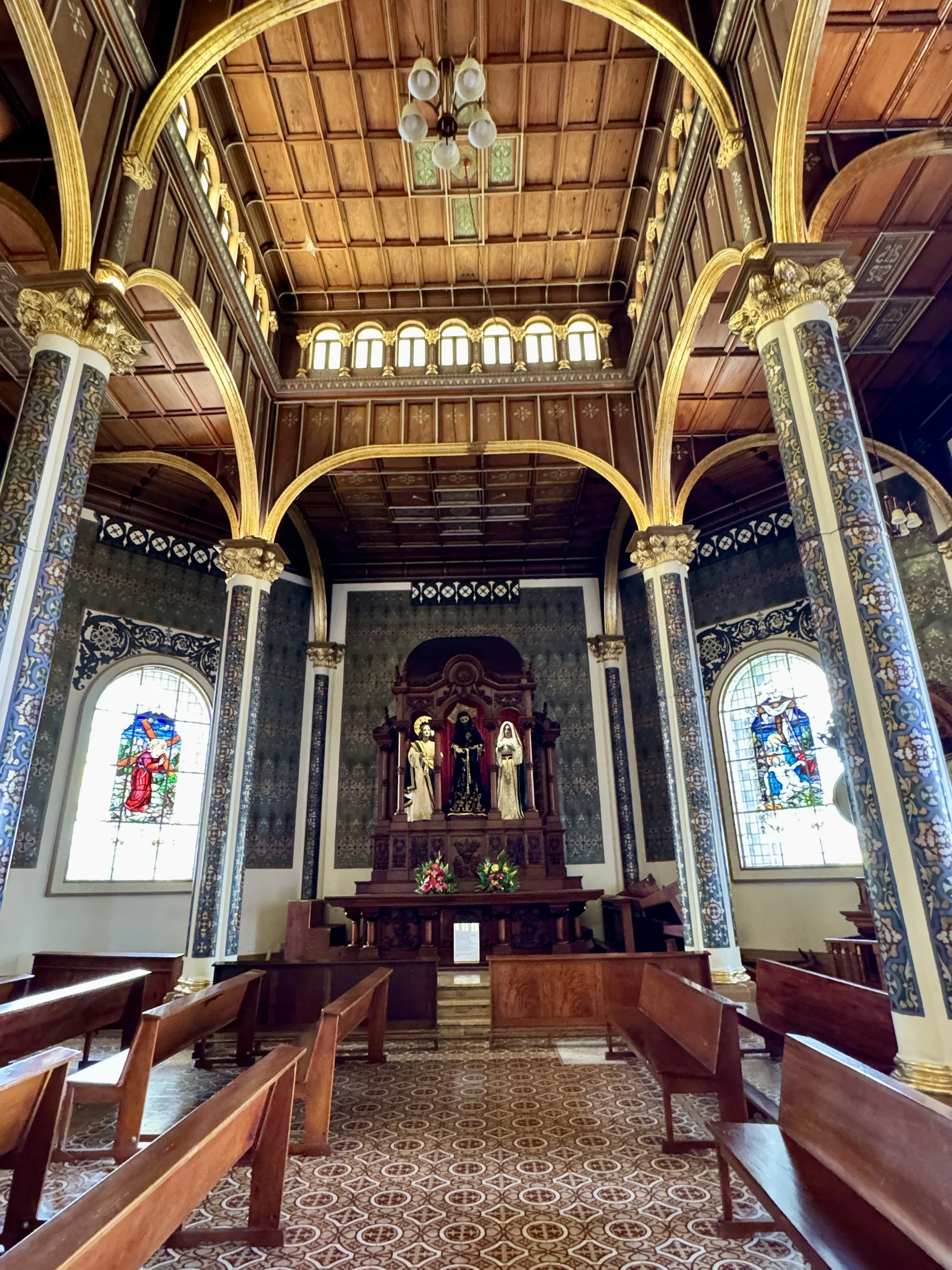 Interior of the basilica showing wooden ceiling, marble columns, altar, and rows of pews.