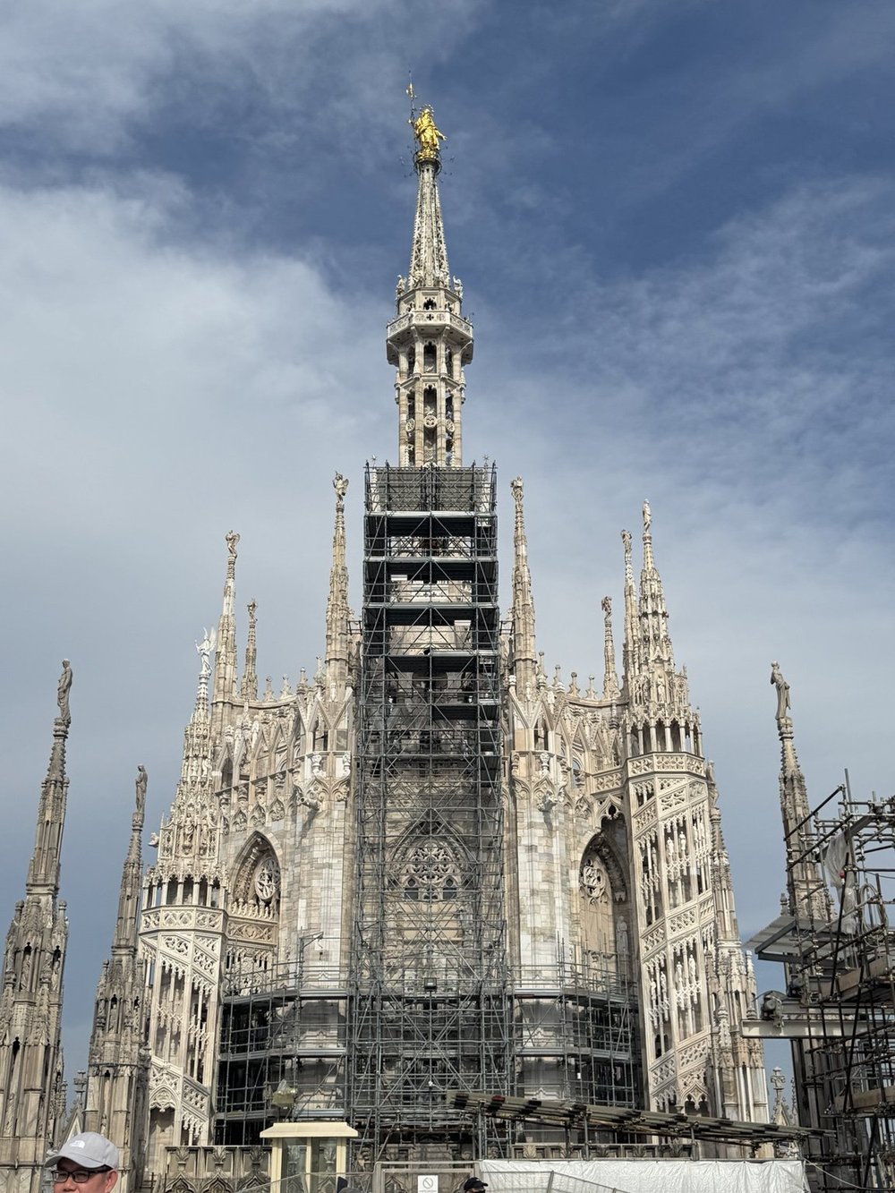 Golden Madonnina statue above the central spire and restoration scaffolding on the Duomo di Milano rooftop.