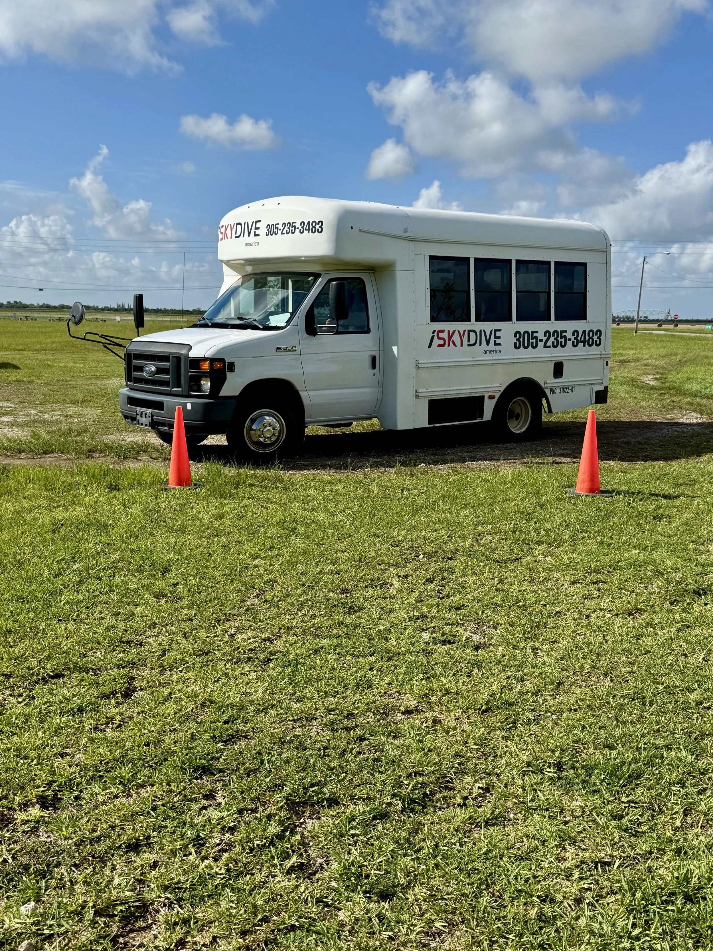white shuttle bus parked on the grass near the drop zone with orange cones