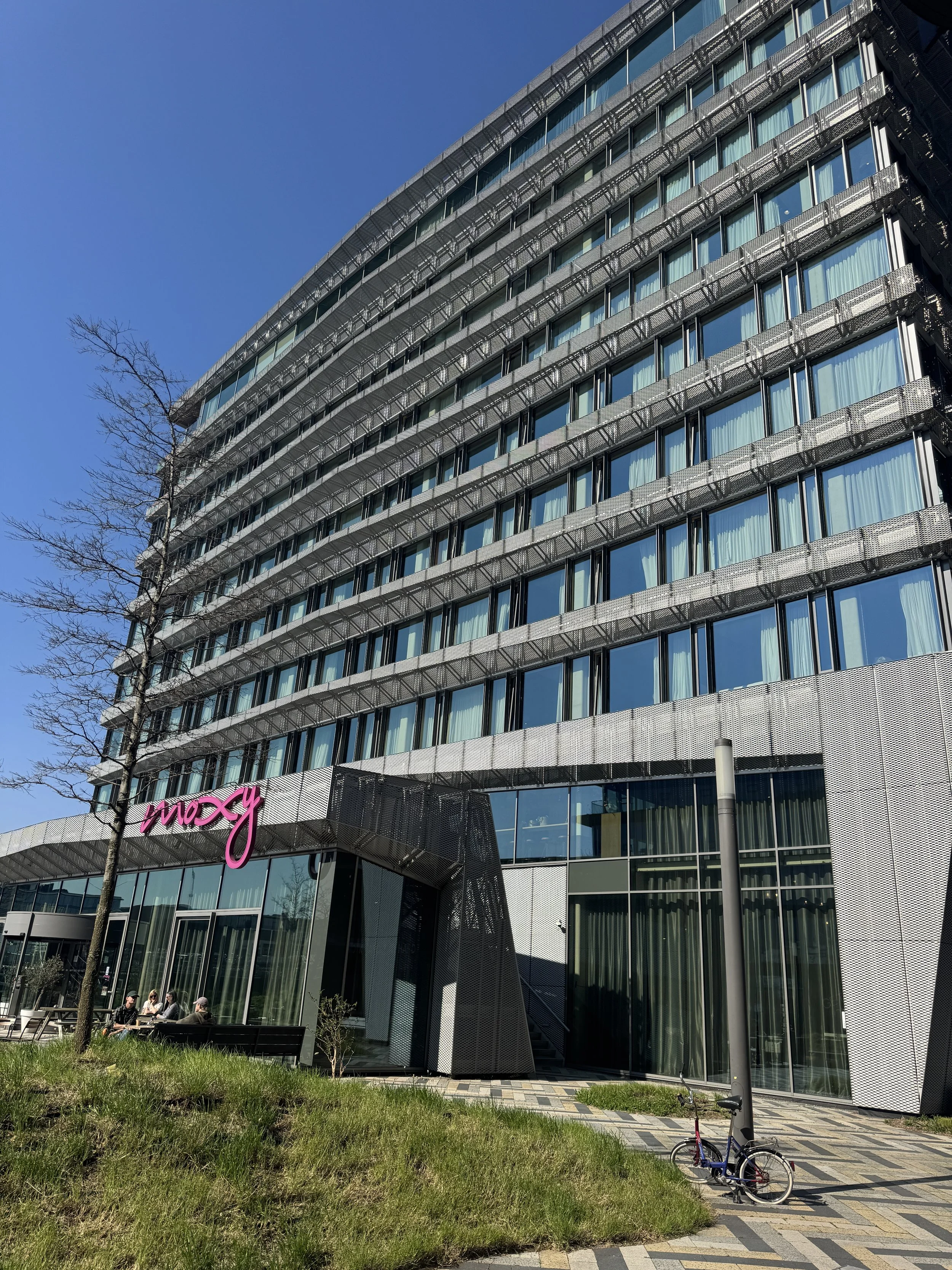 Modern exterior of Moxy Amsterdam hotel with glass facade and multi-story structure on a sunny day
