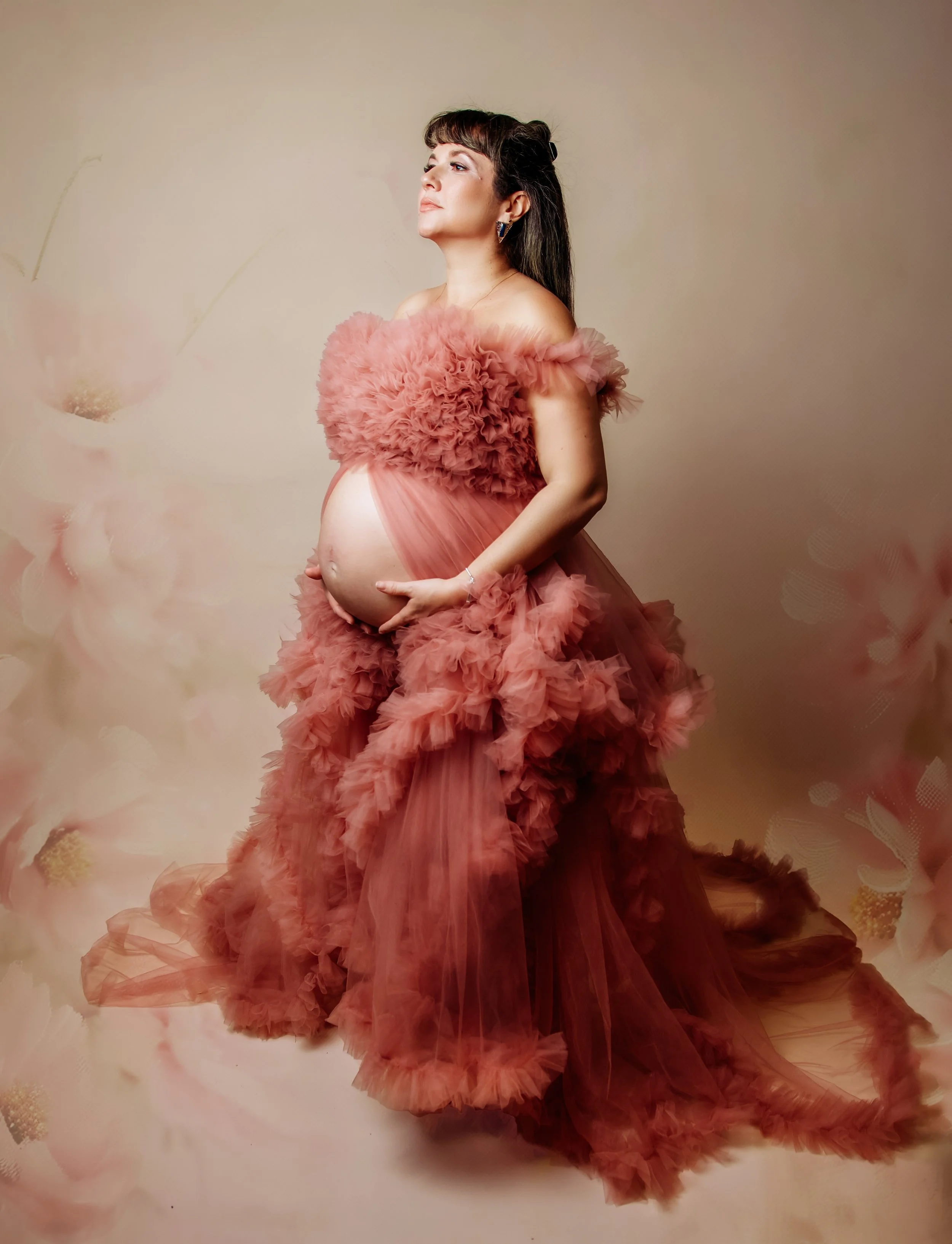 Pregnant woman in a pink ruffled gown with floral background