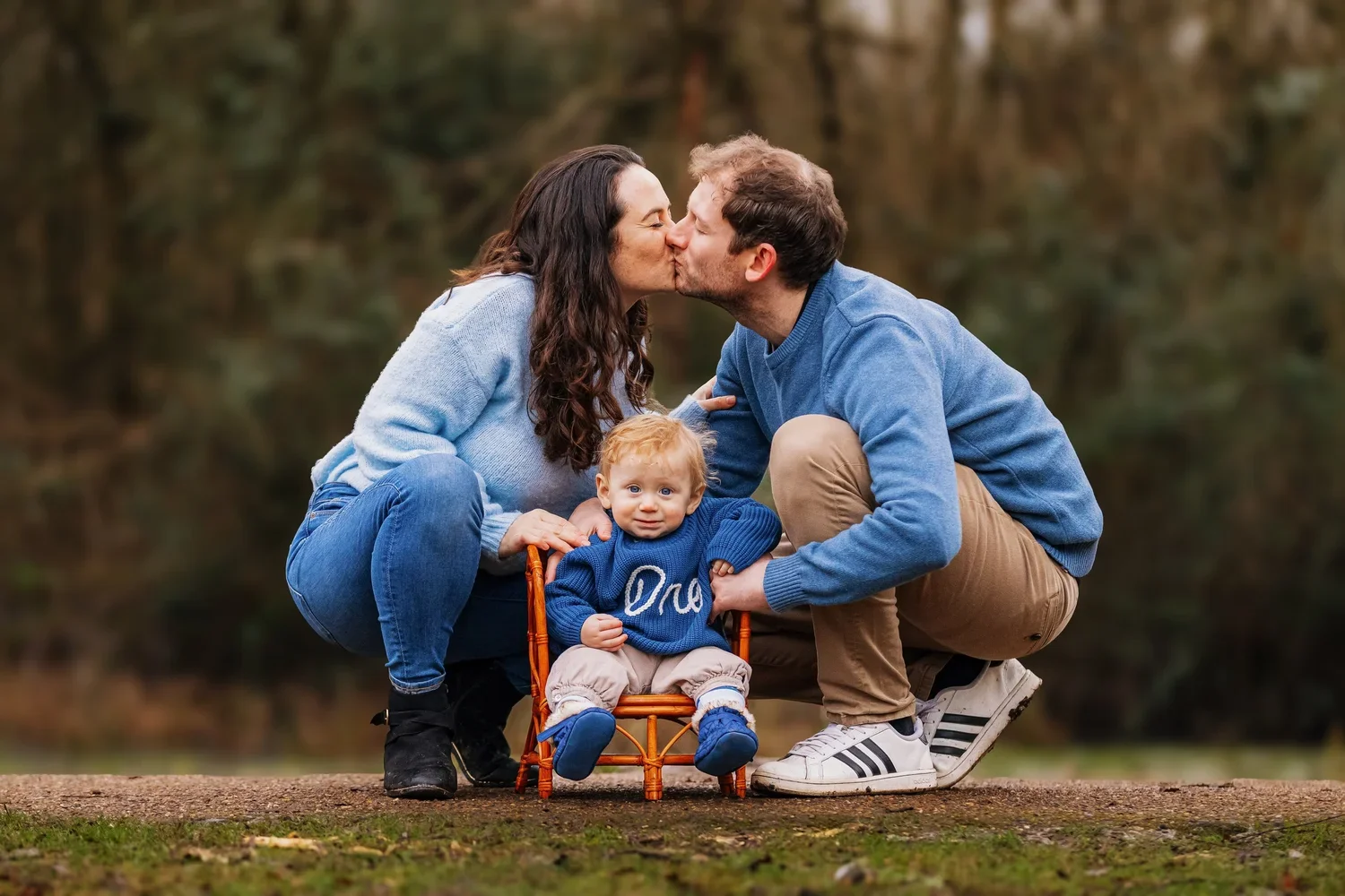 Family portrait outdoors in Surrey with parents kissing while their young child sits between them