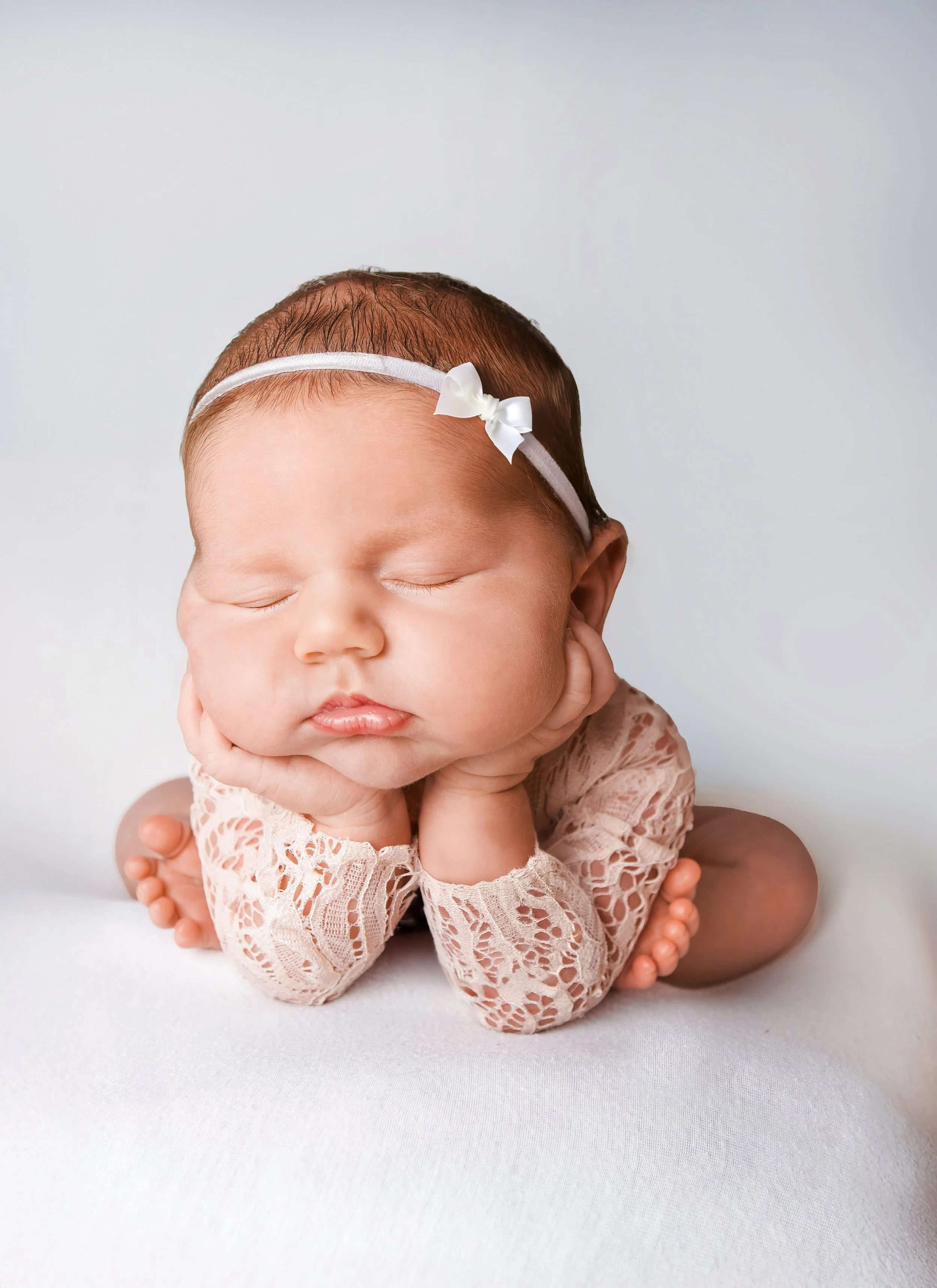 newborn girl with white floral headband in froggy pose position on a soft white background newborn studio photoshoot