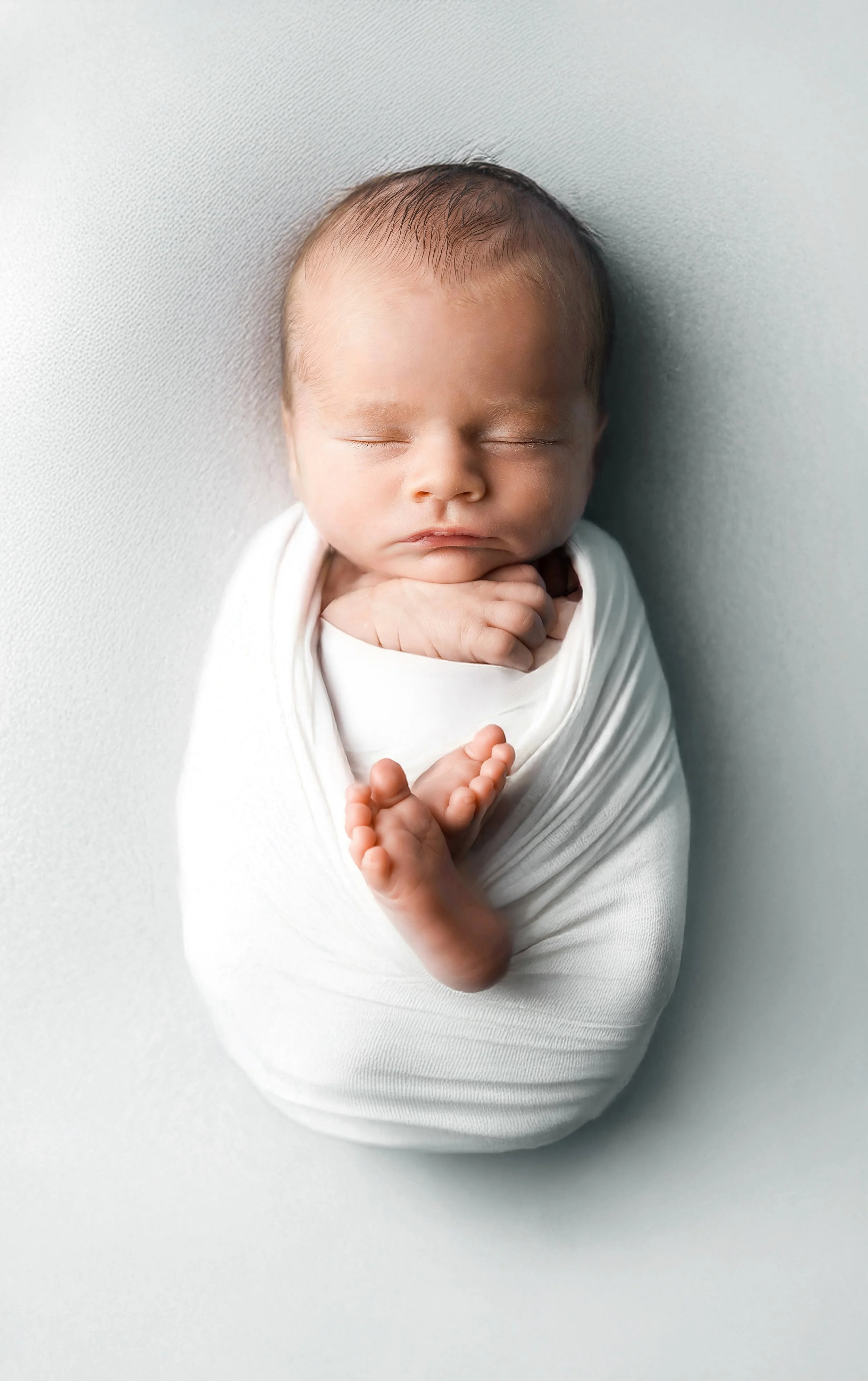 newborn shoot of a boy wrapped in white with white backdrop