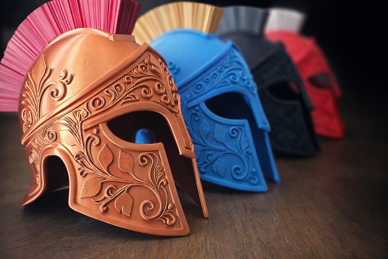 Four ornate gladiator-style helmets in copper, blue, black, and red, each with a decorative crest, arranged in a row on a wooden surface.
