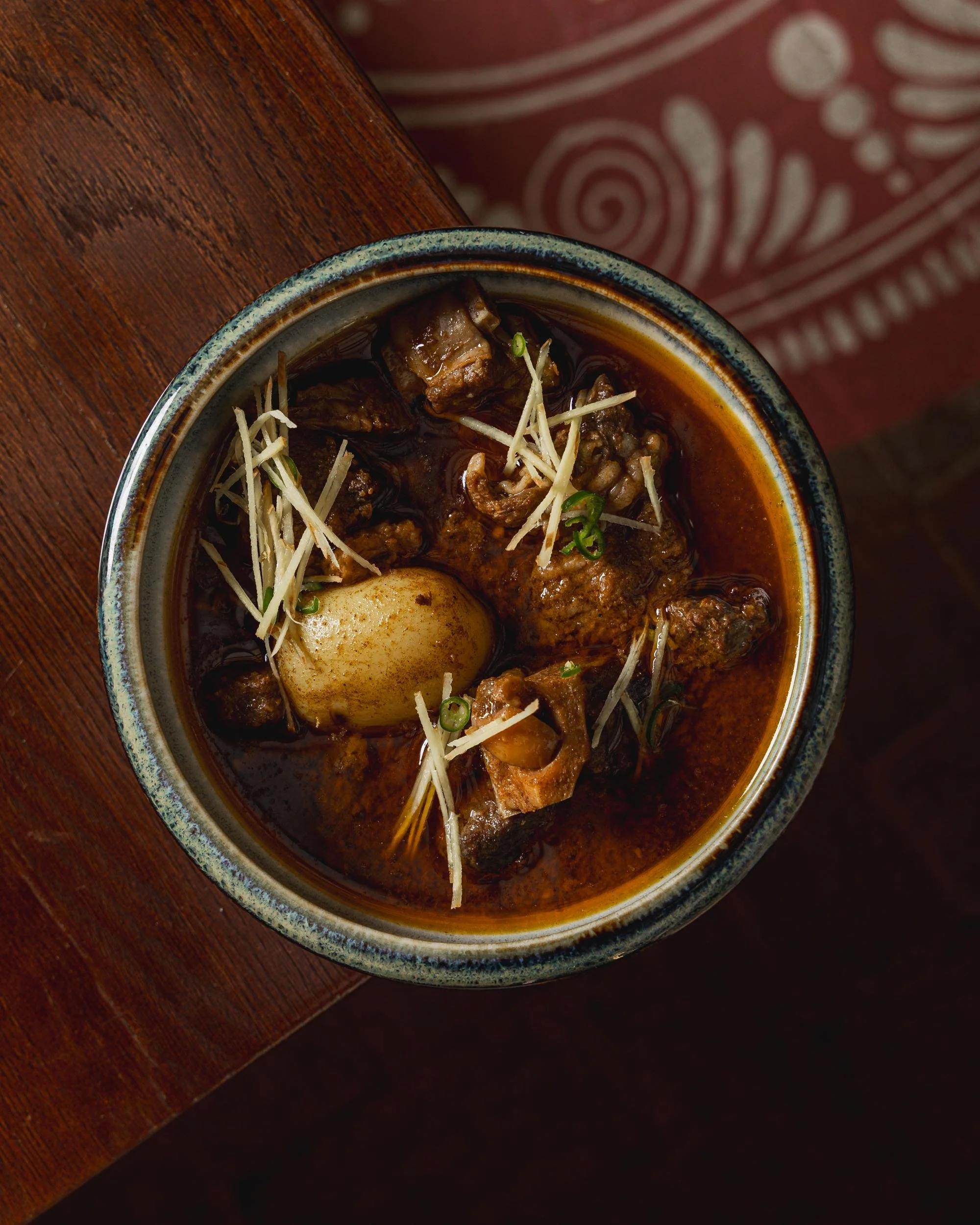 A bowl of steaming beef stew with chunks of beef, a whole boiled egg, topped with sliced ginger and chopped green onions.