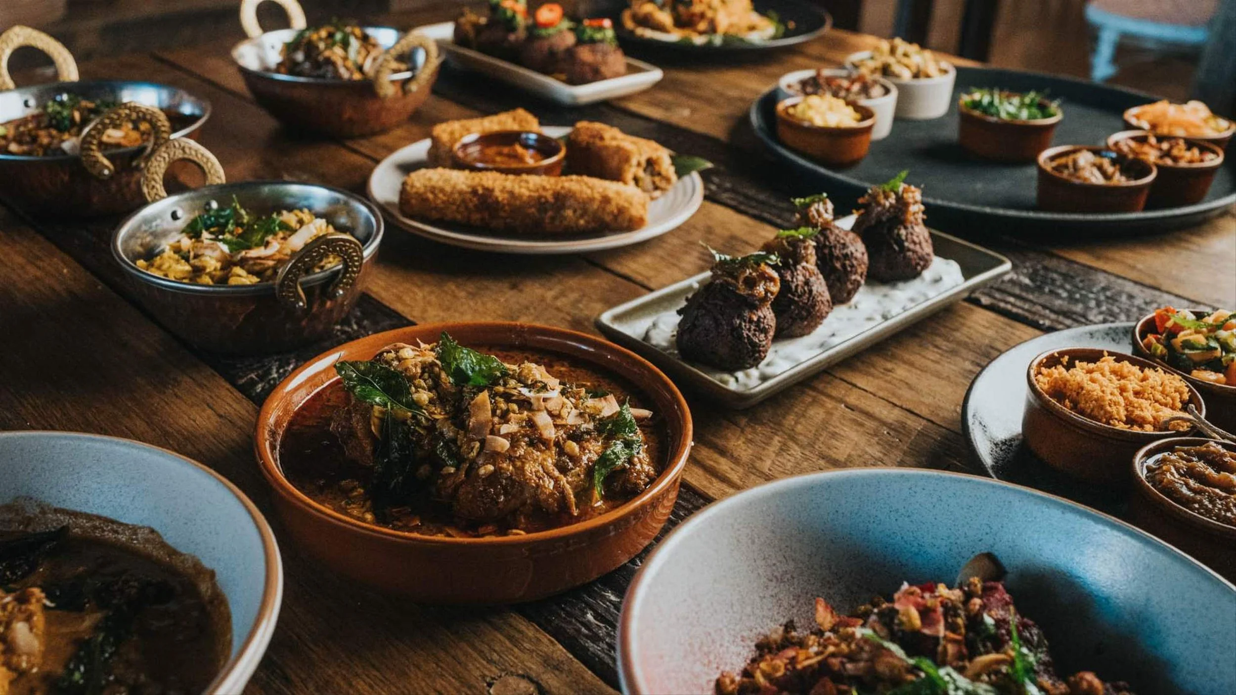 A variety of Mexican dishes on a rustic wooden table including meats, rice, and vegetable side dishes in colorful bowls and plates.