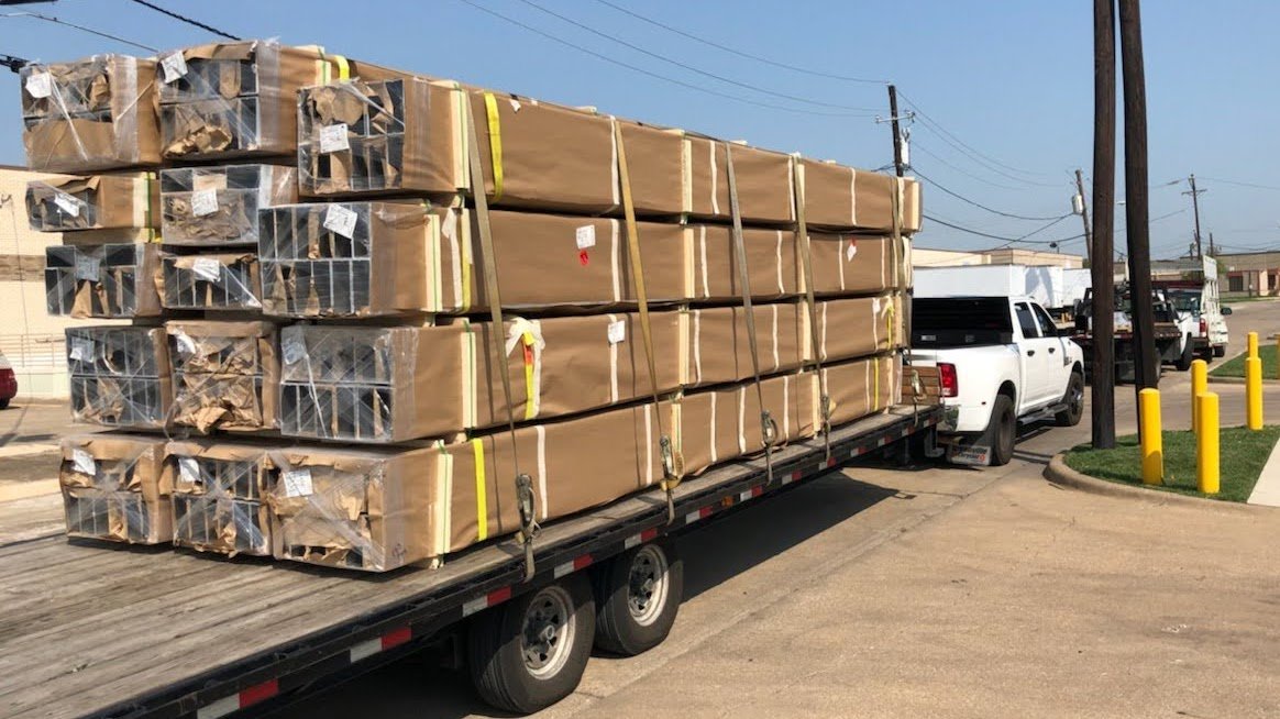 A flatbed truck carrying large, wrapped packages secured with straps.