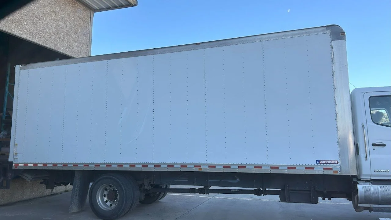 A white box truck parked next to a building with a cloudy sky in the background.