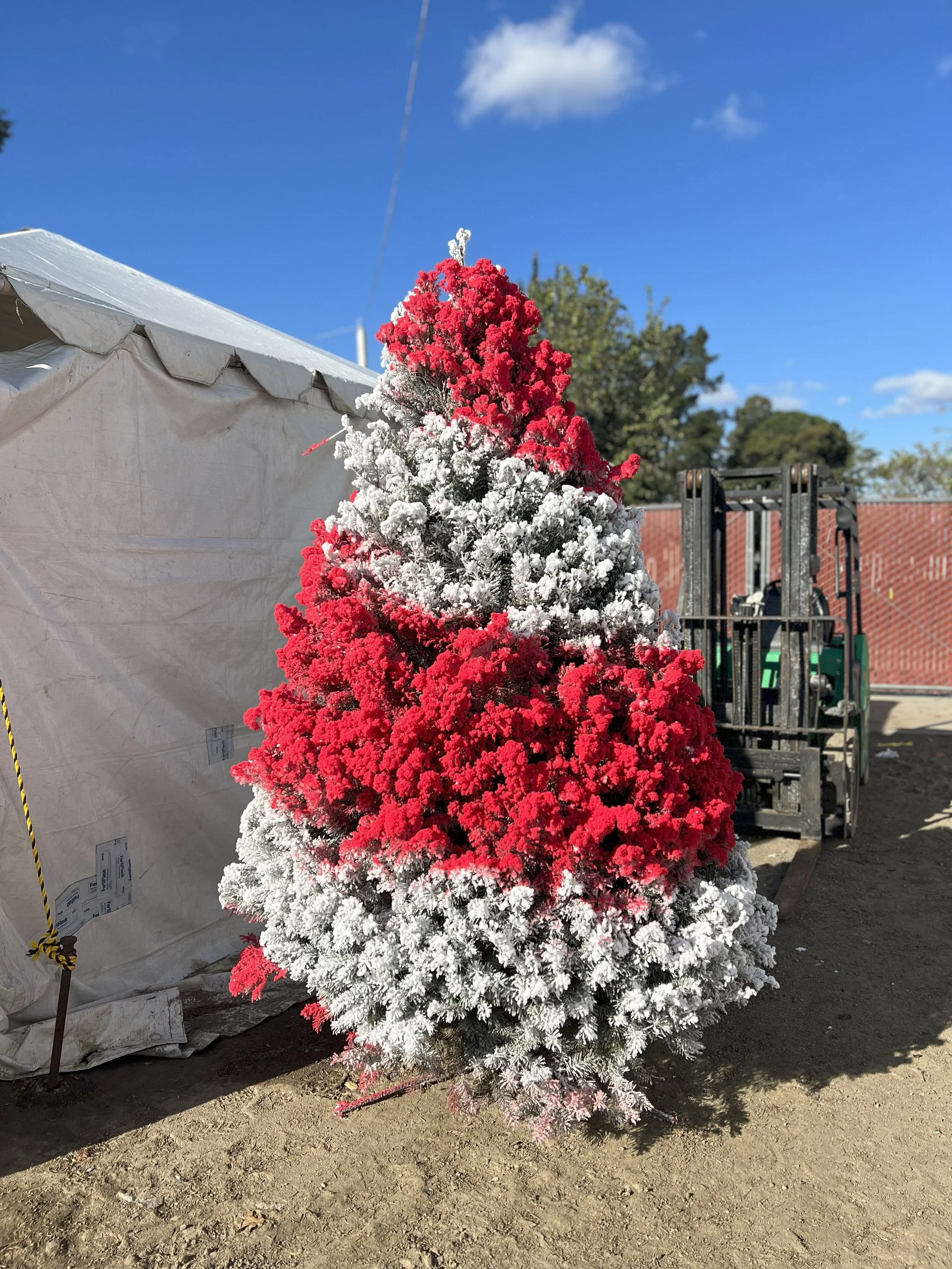 Colorful flocked Christmas tree with red and white swirled branches outdoors on a sunny day.