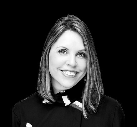 Black and white photo of a smiling woman with shoulder-length hair, wearing a dark top and a patterned scarf, against a plain background.