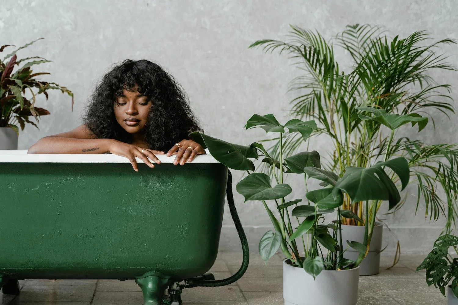 Black woman resting in a green bathtub, surrounded by plants—reflecting calm, personalized care in a home birth team setting.