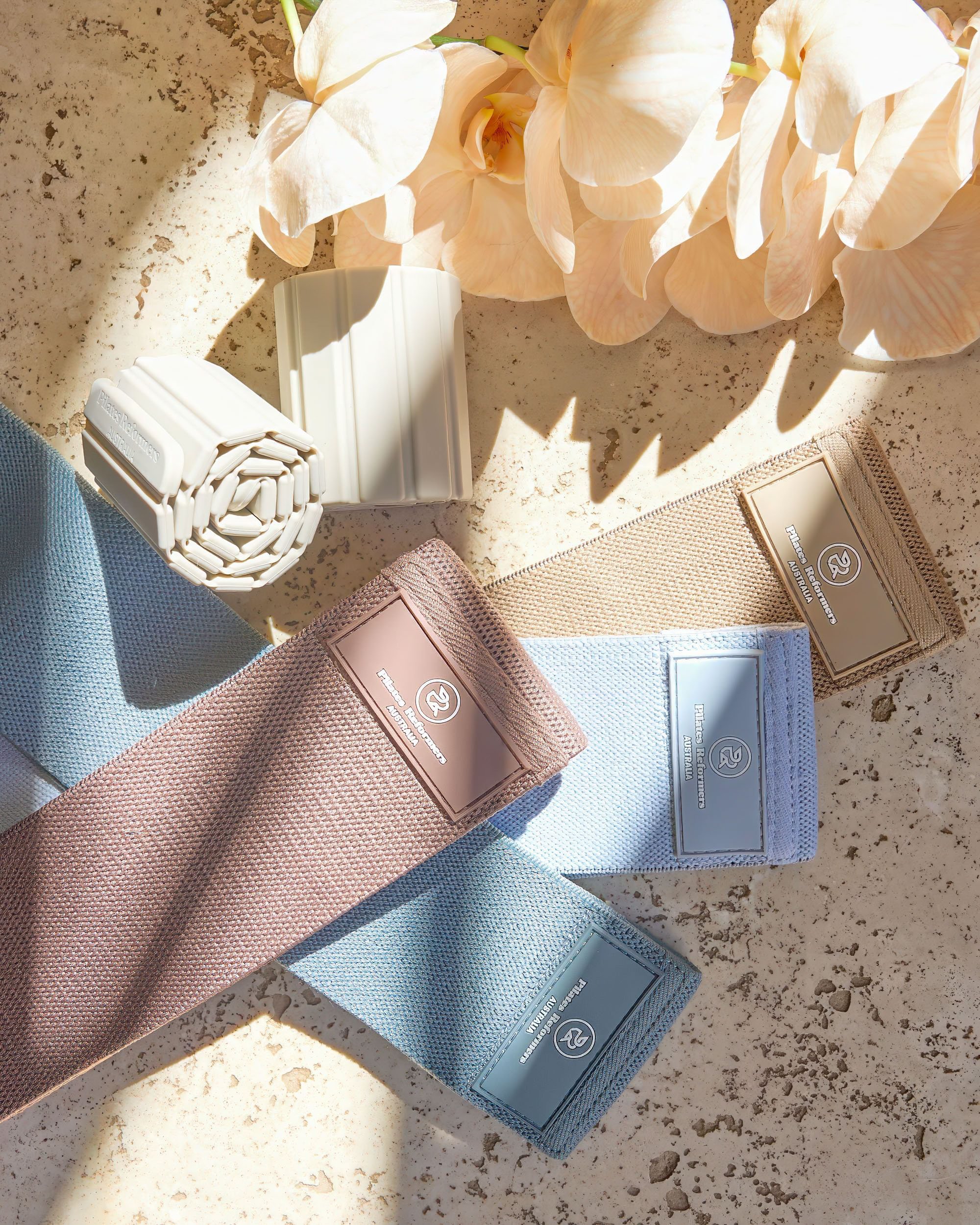 Colorful elastic bands with labels, cream-colored flowers, and a rolled-up white item on a speckled surface.
