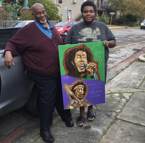 Two collectors holding a Bob Marley painting