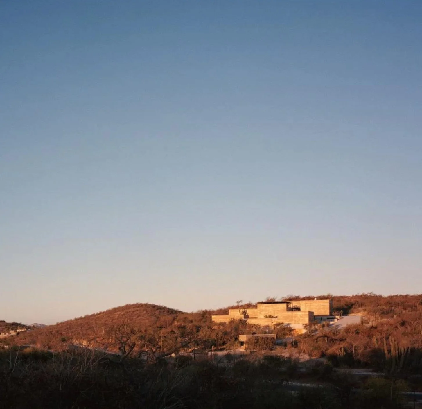 Hills of San José del Este sparse desert vegetation and modern beige buildings under a clear blue sky at sunrise or sunset.
