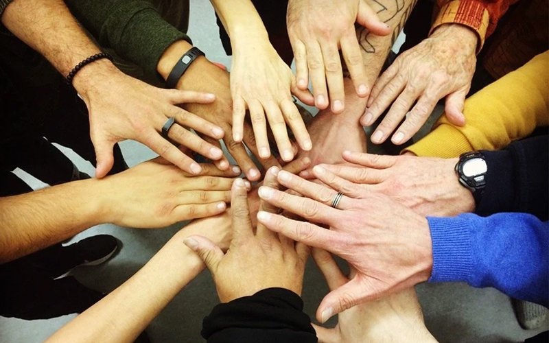 Multiple diverse hands placed together in a circle, all reaching toward the center, symbolizing unity and teamwork.