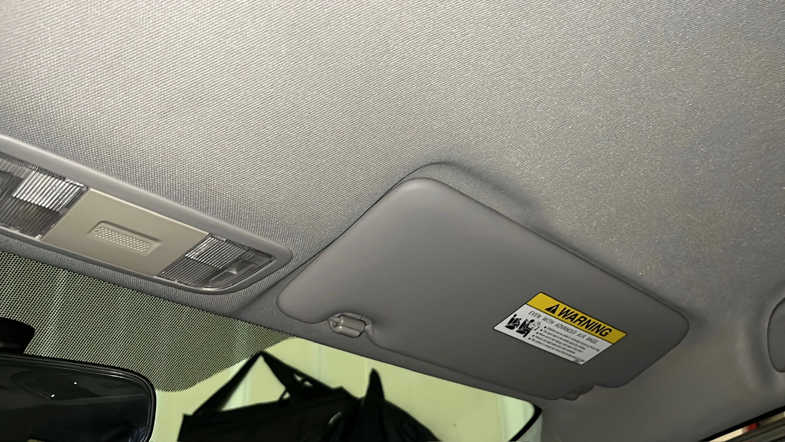 Car's interior ceiling featuring a built-in overhead light, a warning label on the sun visor, and part of the rearview mirror.