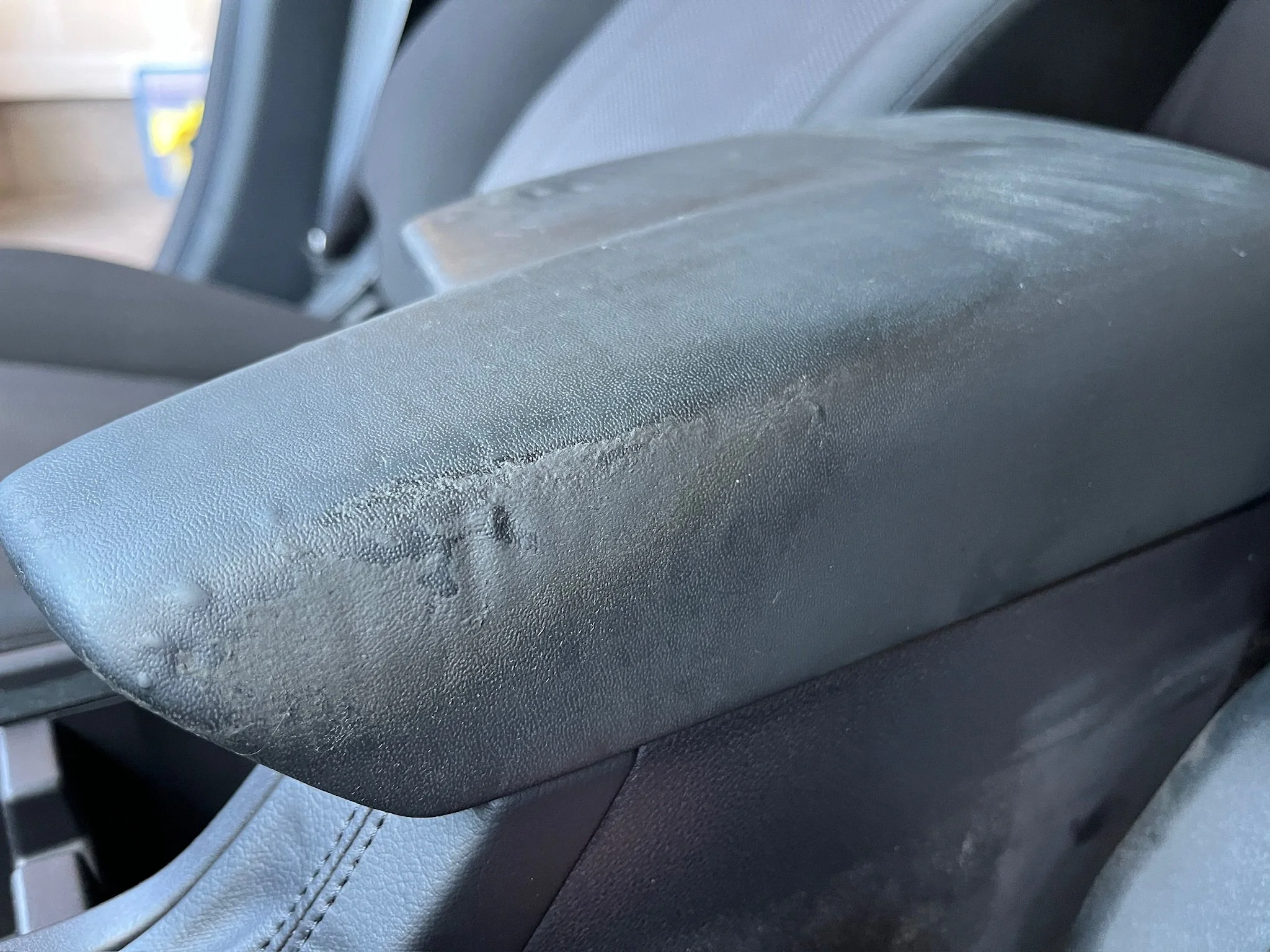 Close-up of a black car armrest with visible scratches and scuffs.