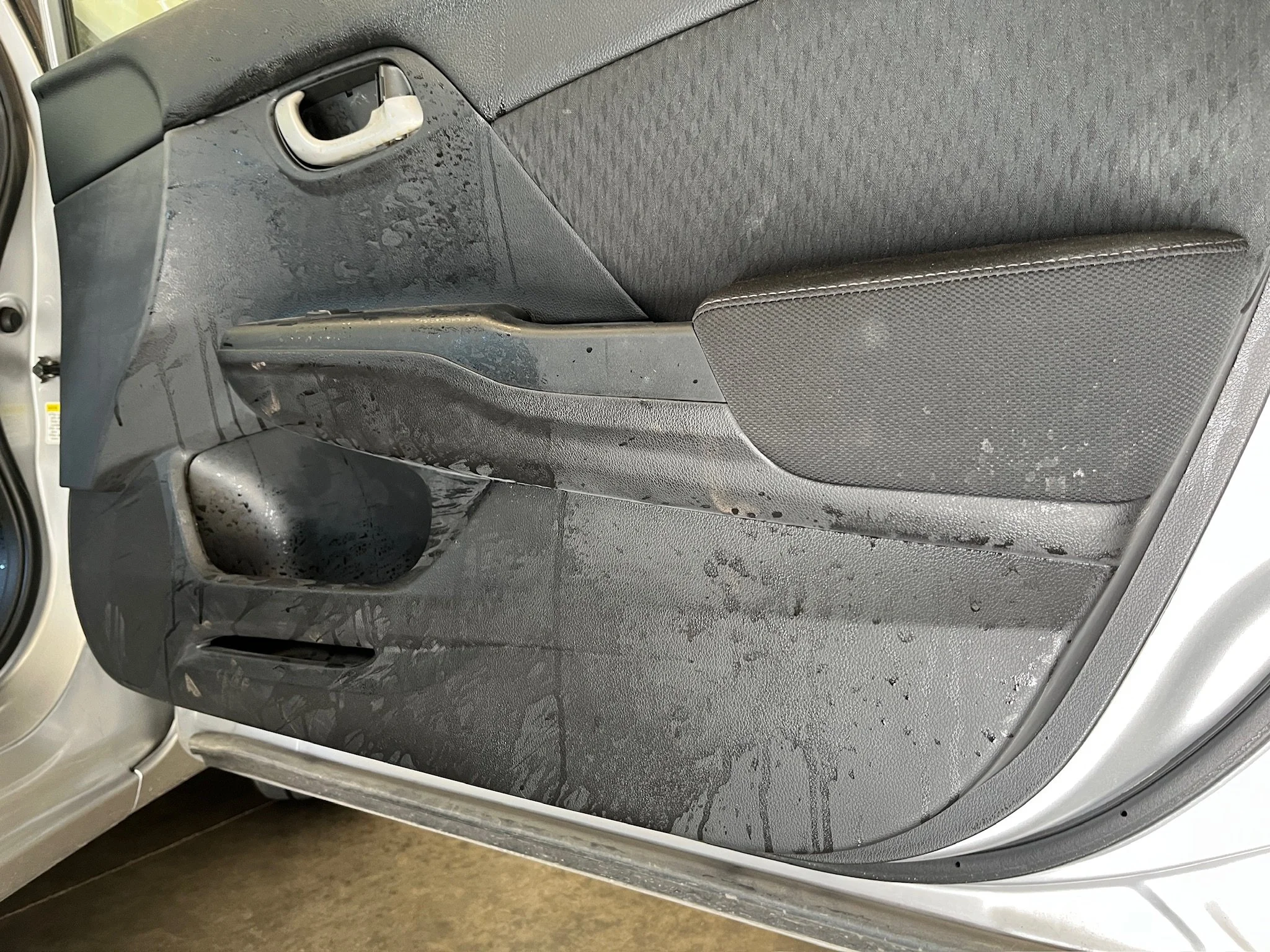 Car door interior with water or liquid stains and dirt on the surface.