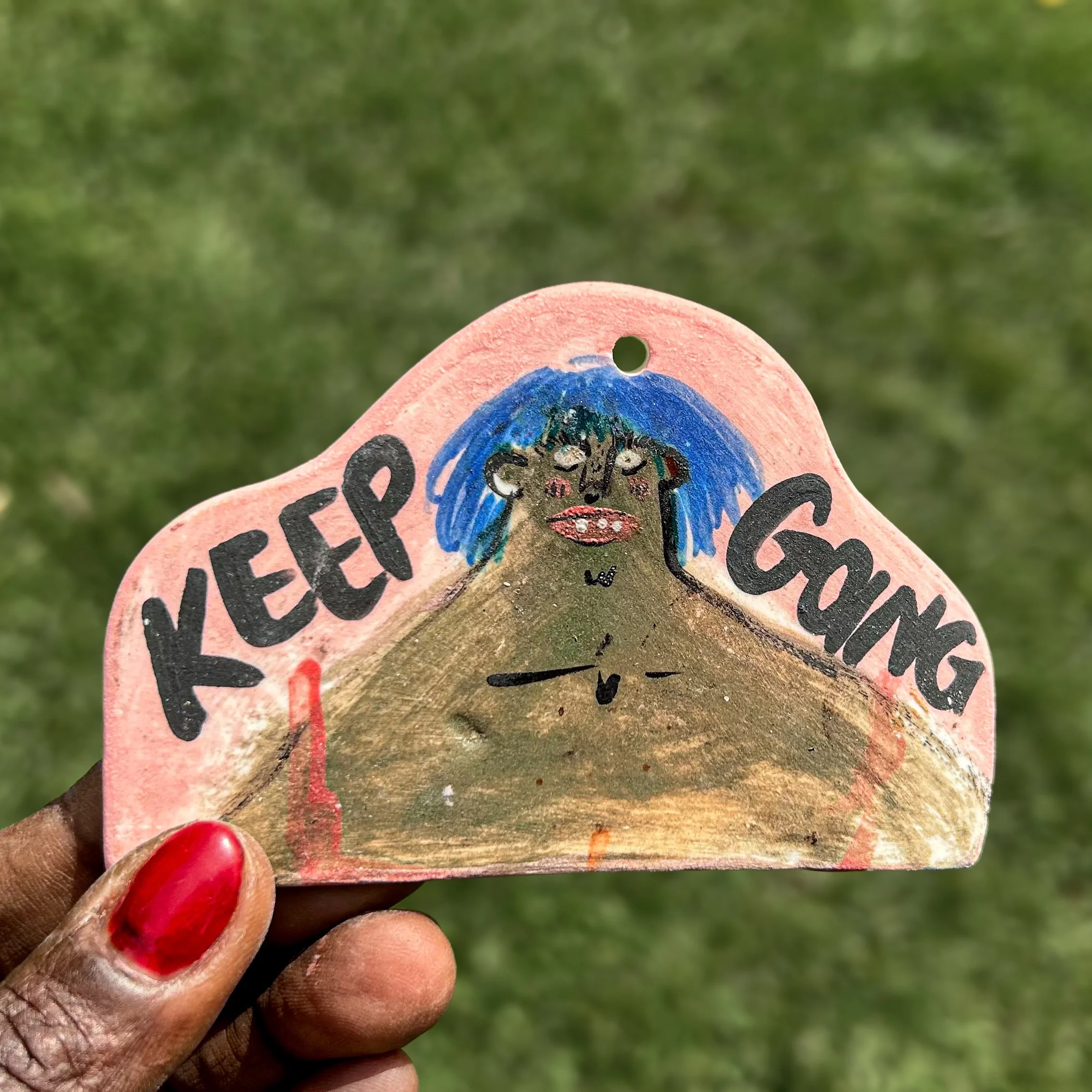 A small wall ornament with a chubby bust woman, blue hair with (Keep going) text