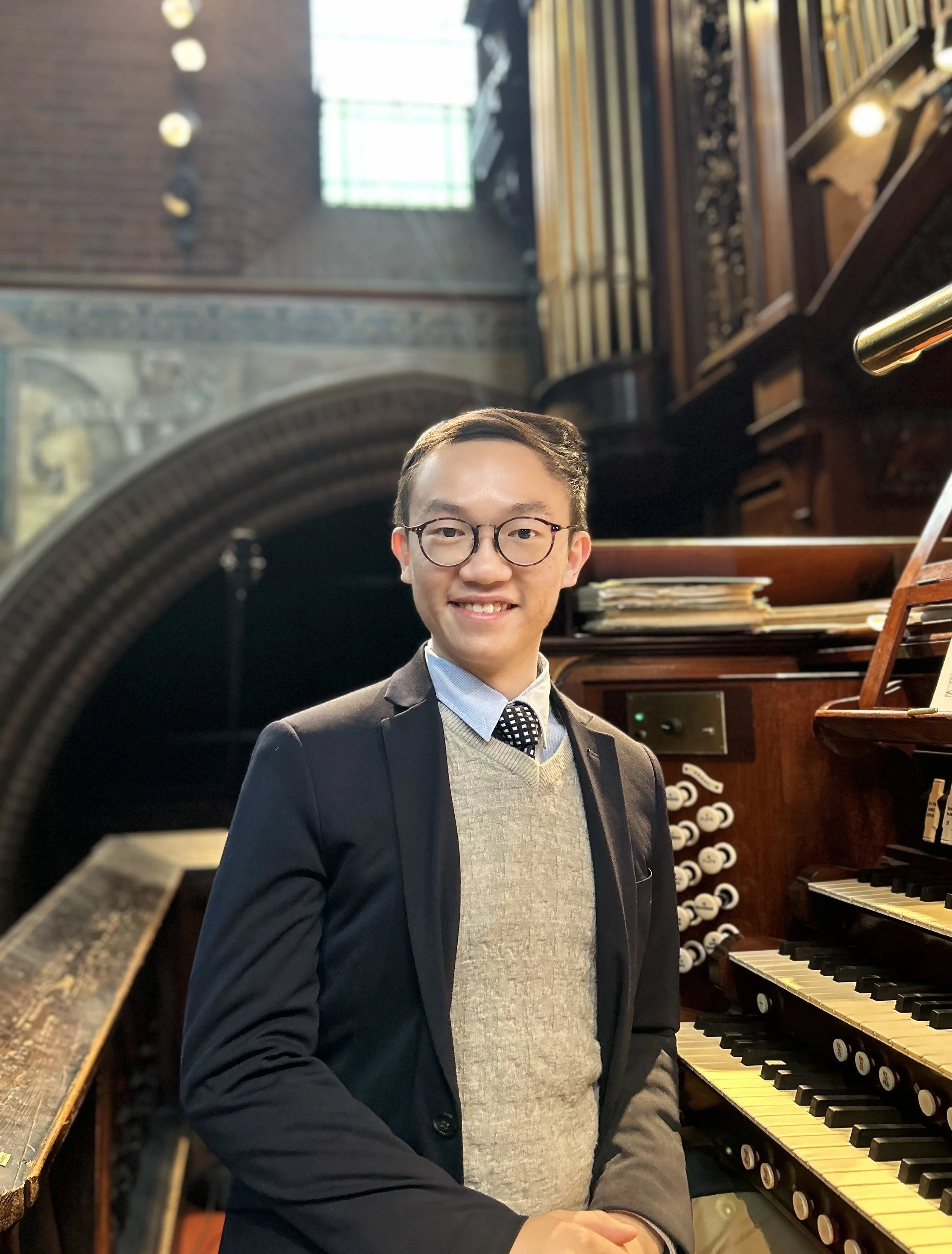 A man in a suit and glasses standing in front of a pipe organ in a church or cathedral