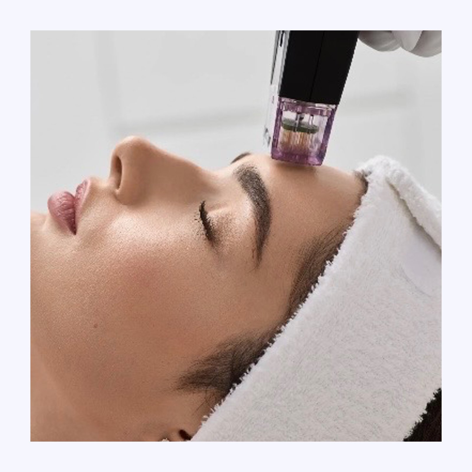 A woman receiving a facial treatment with a cosmetic device applied to her forehead in a spa setting.