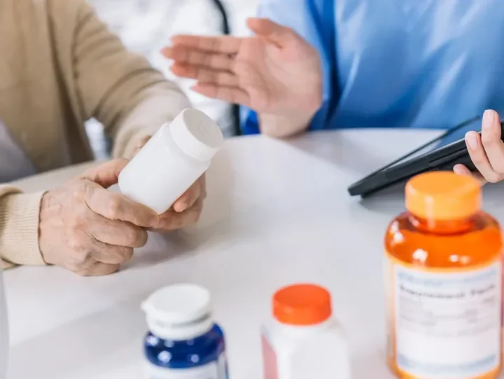 A healthcare professional handing medication bottles to an elderly patient during a consultation.