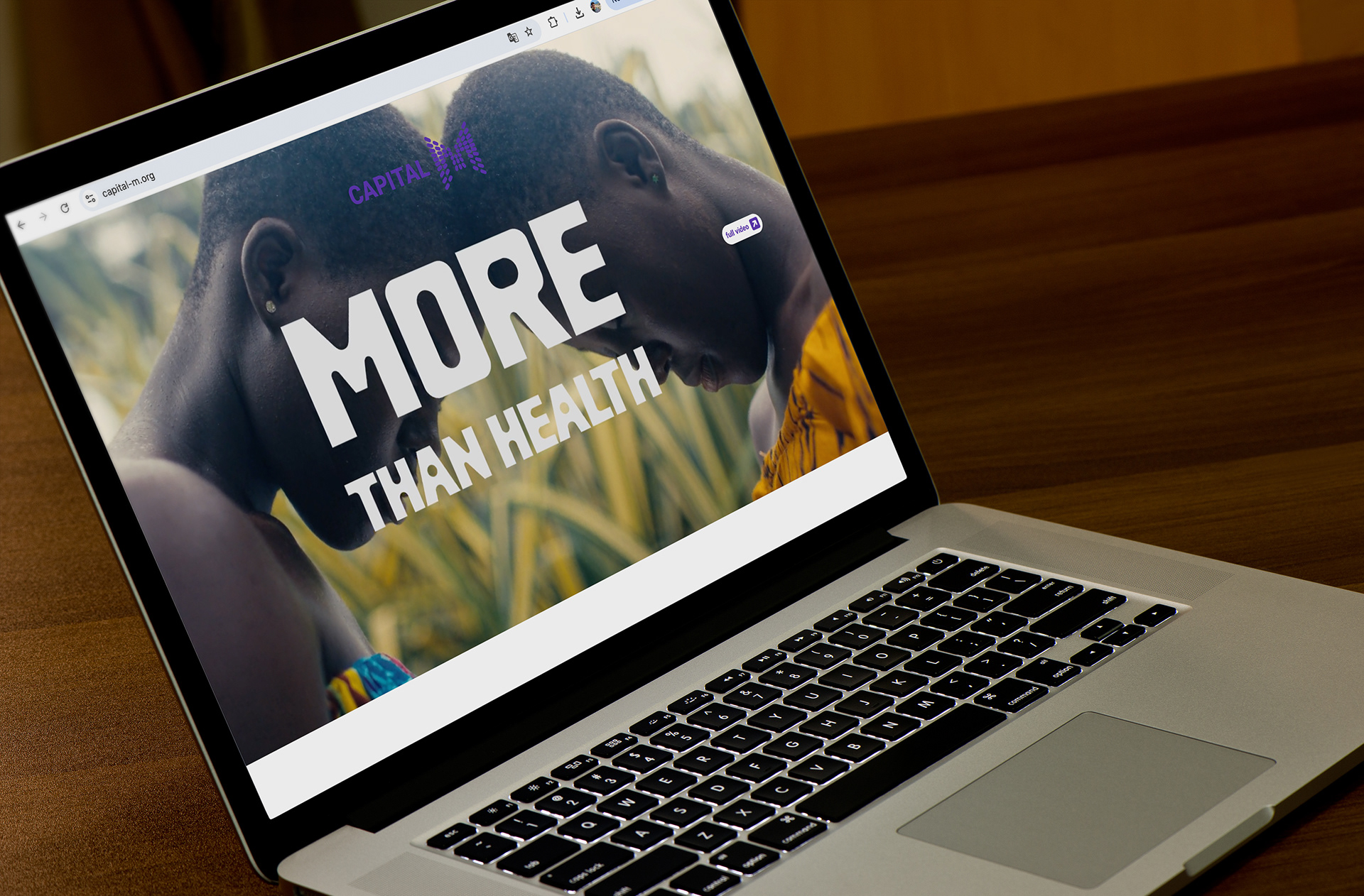 Laptop displaying a website with the text 'MORE THAN HEALTH' over an image of two people, one with short curly hair and another with a shaved head, in an outdoor setting.