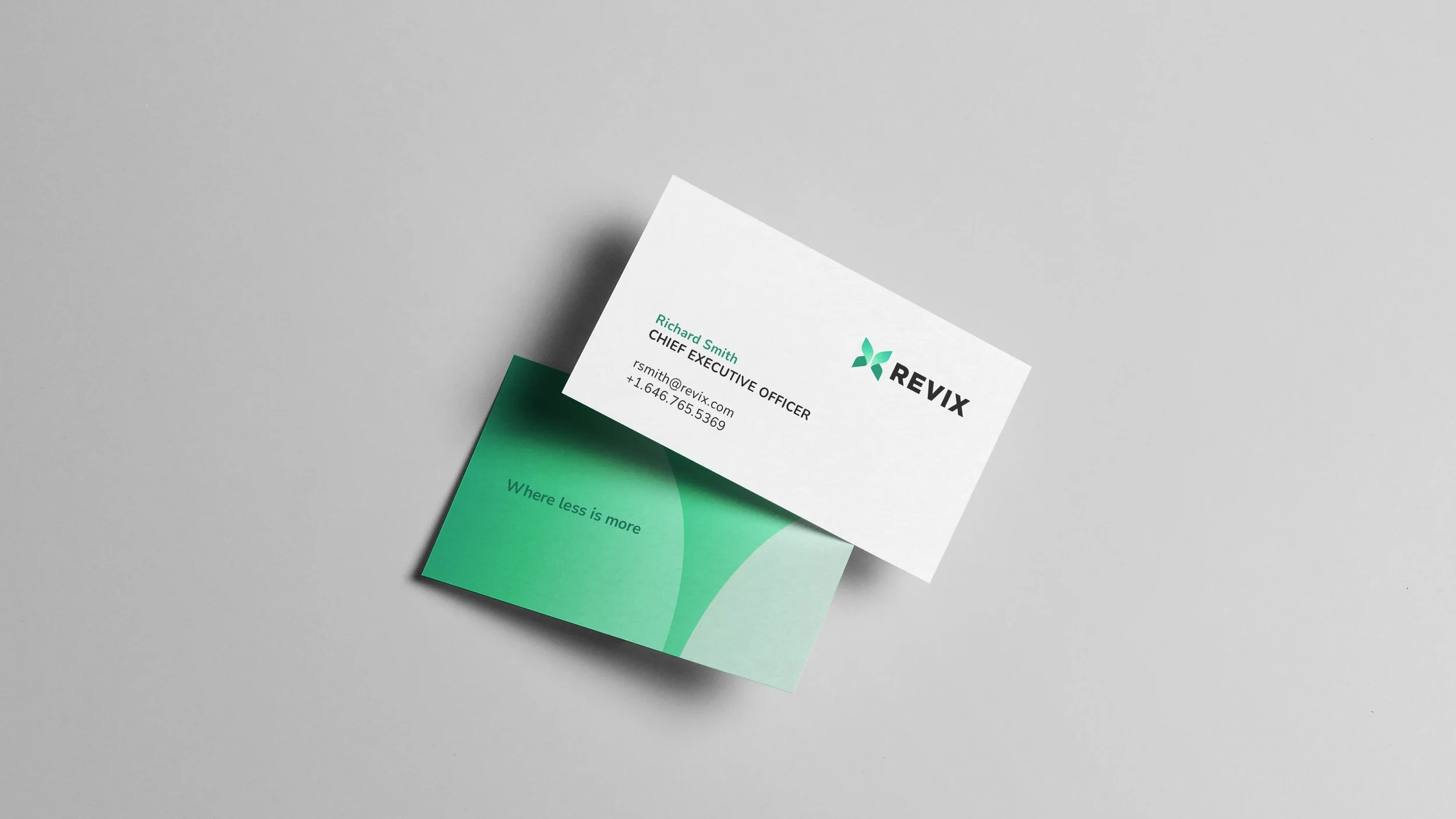 A white business card with the REVIX logo, the name Richard Smith, title Chief Executive Officer, email address rsmith@revix.com, and phone number +1.646.765.5369, placed on top of a green card with the message "Where less is more," on a gray surface.