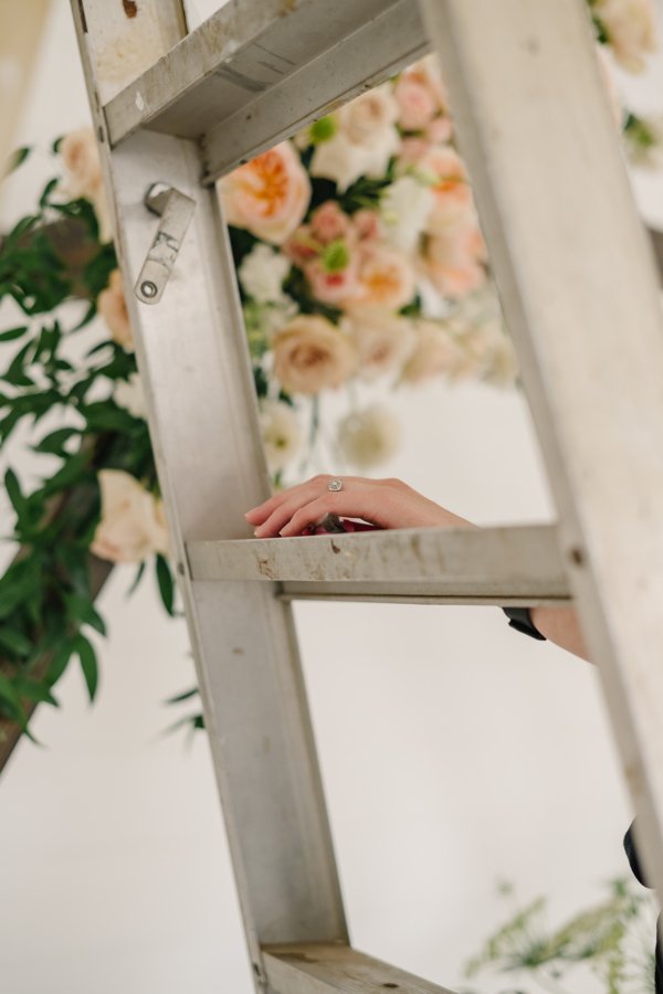 How Much Do Wedding Flowers Cost In Utah? (Photo of a Utah wedding florist's hand resting on a ladder, with a design in the background).