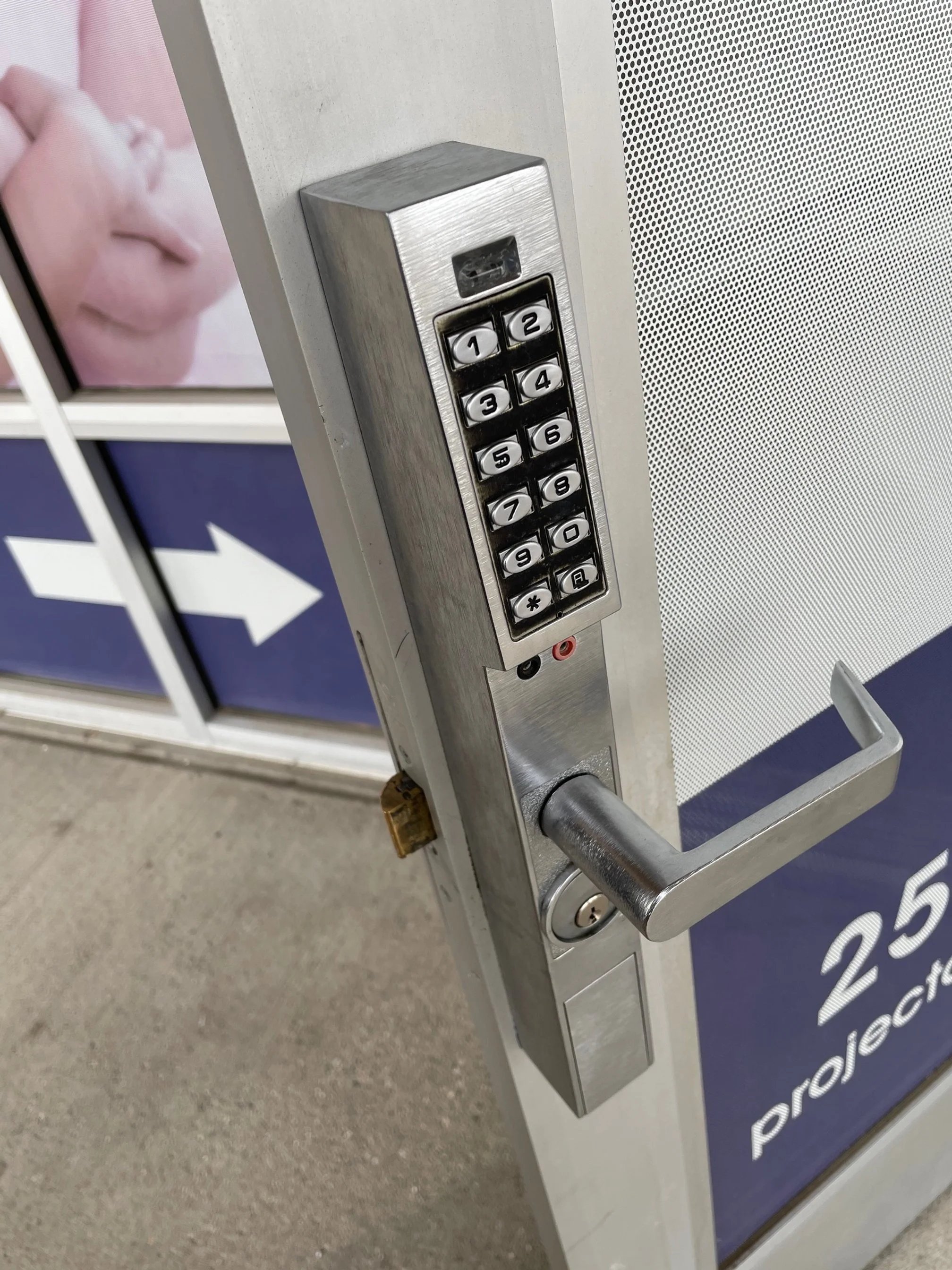 A locked door with a combination keypad lock and handle, located near a sign with a blue background and white arrow.