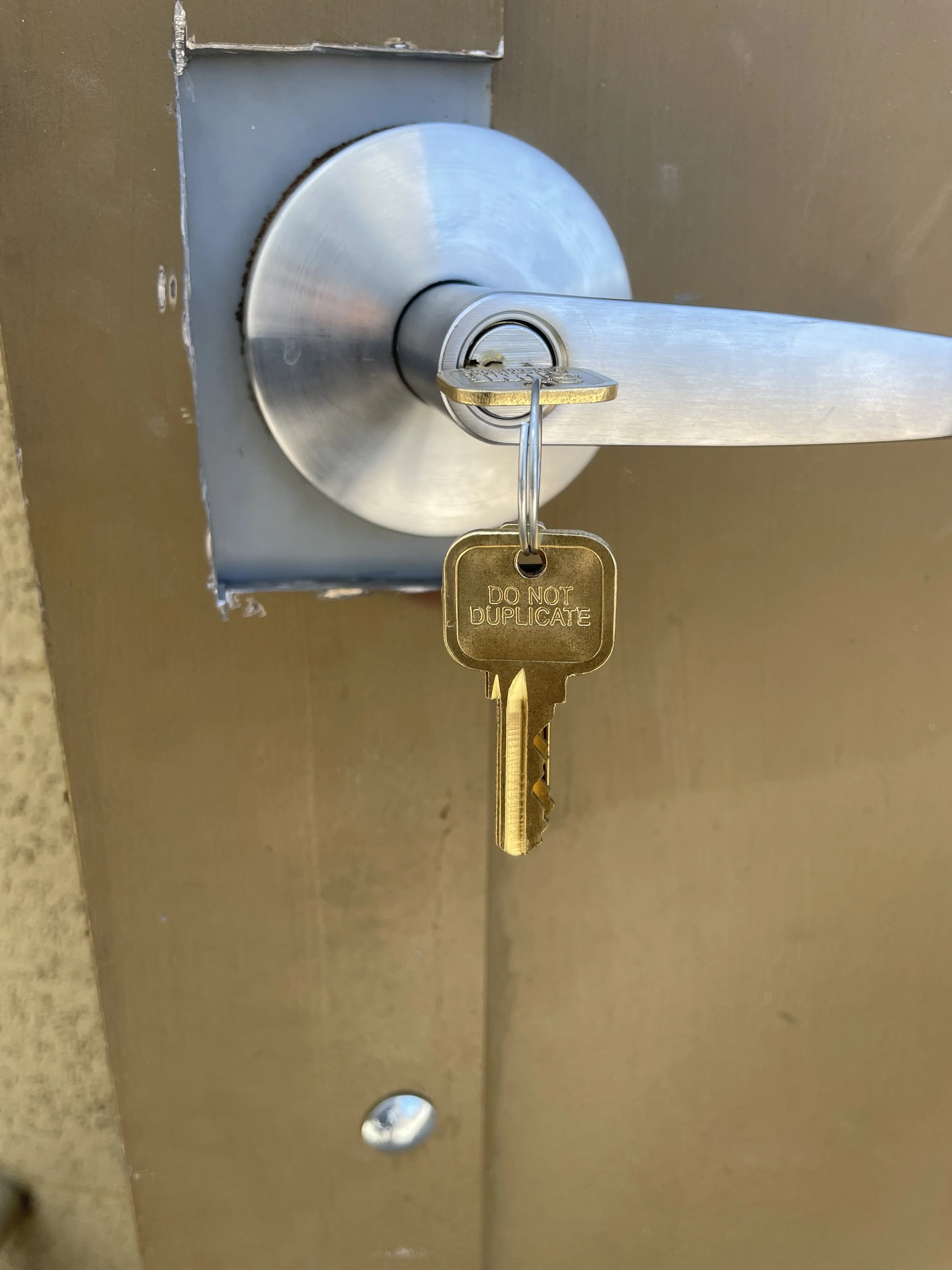 Close-up of a silver door handle with a key inserted, hanging on a key ring with a gold key that has the words 'DO NOT DUPLICATE' engraved on it.