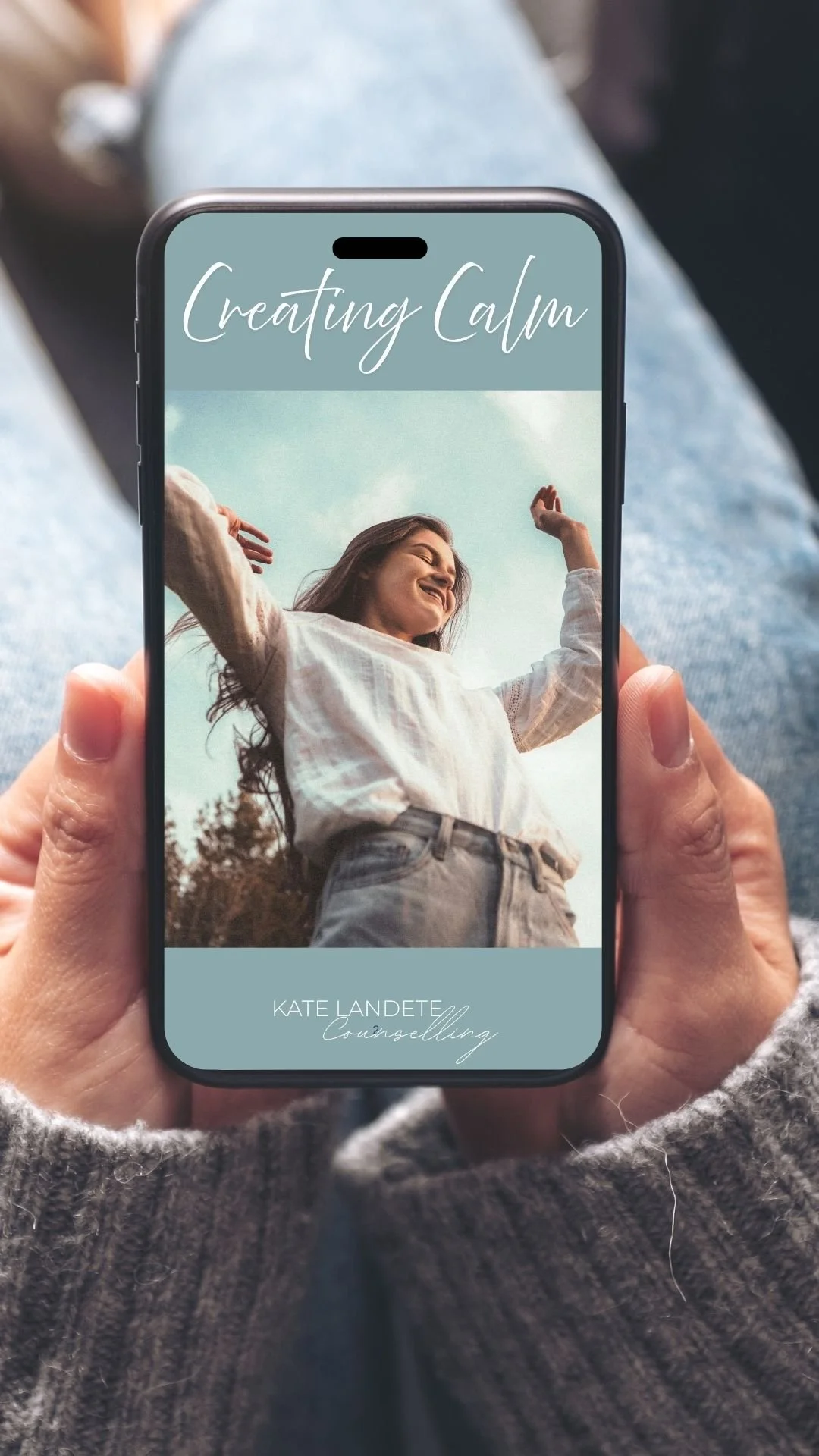 A person holding a smartphone displaying a calming image of a smiling woman with arms raised against a sky with text 'Creating Calm' and 'Kate Landete Counselling'.